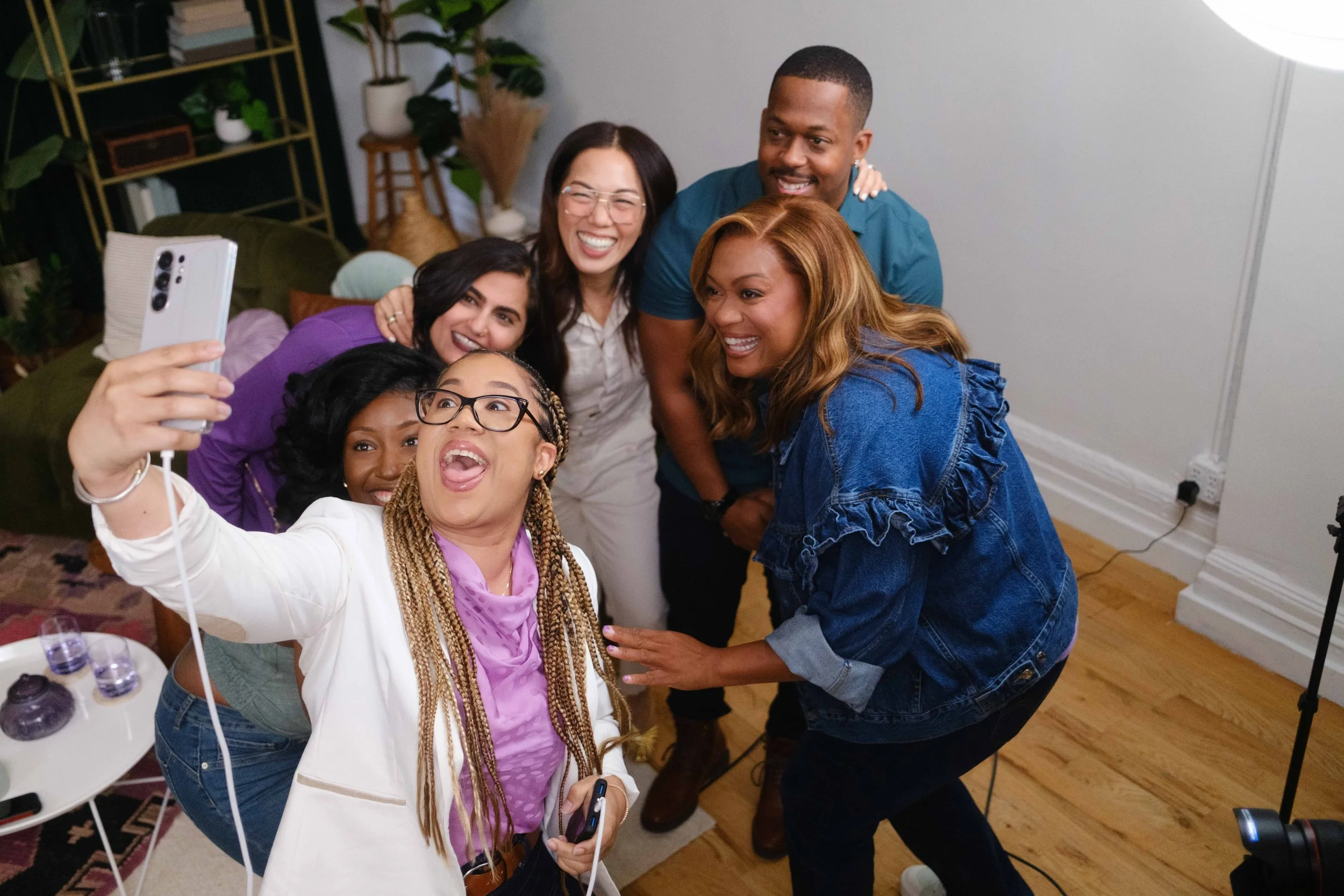 Group of seven diverse friends taking a selfie together in a cozy indoor setting, smiling and enjoying each other's company.