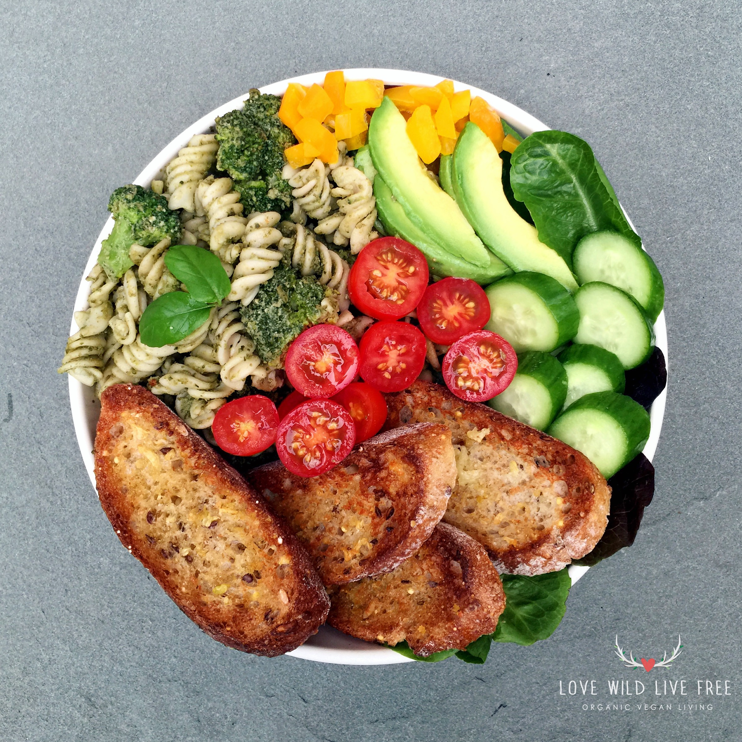 The BEST Vegan Garlic Bread, served with homemade pesto pasta and broccoli, mixed greens, avocado, cherry tomatoes, yellow peppers and cucumbers. Photo by Love Wild Live Free. 