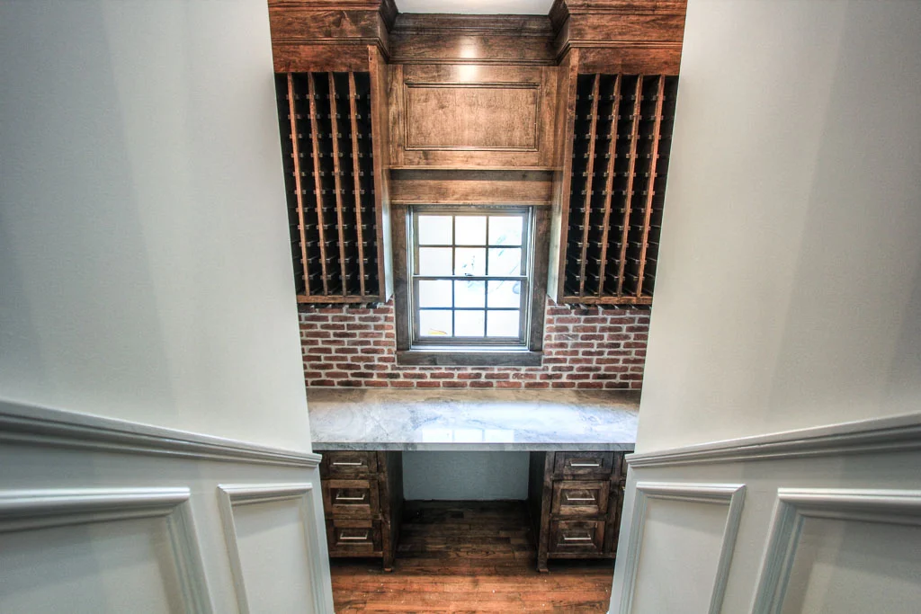 The sunken wine room fully equipped with storage and wine refrigerator. Reclaimed brick backsplash, stained wood cabinets and quartzite counter make this a surprisingly intricate space.