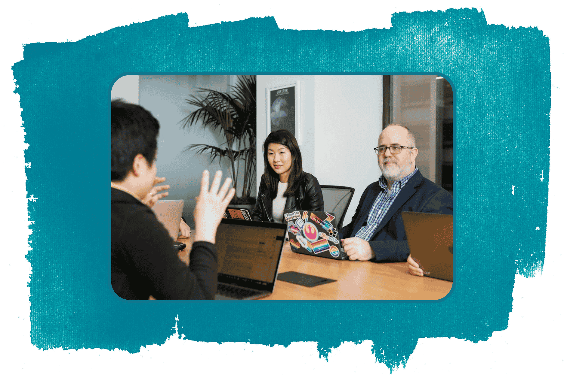 Group of three people having a discussion in a meeting room with laptops, one Asian woman with dark hair, one white man with glasses and a beard, and another person seen from behind. Photo is layered over a large teal paint brushstroke.