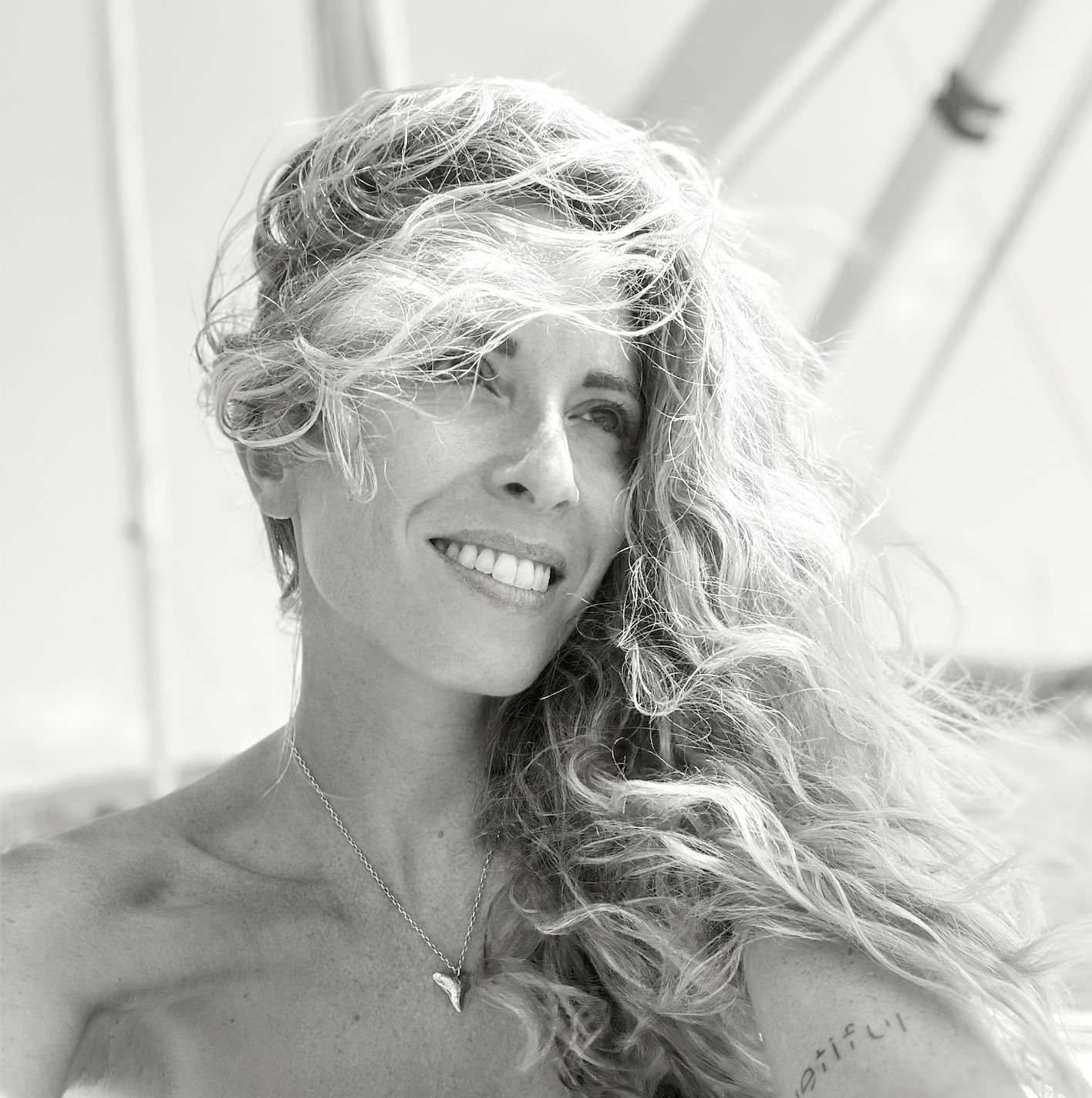 Une femme avec de longs cheveux ondulés, souriante et portant un collier, en noir et blanc.