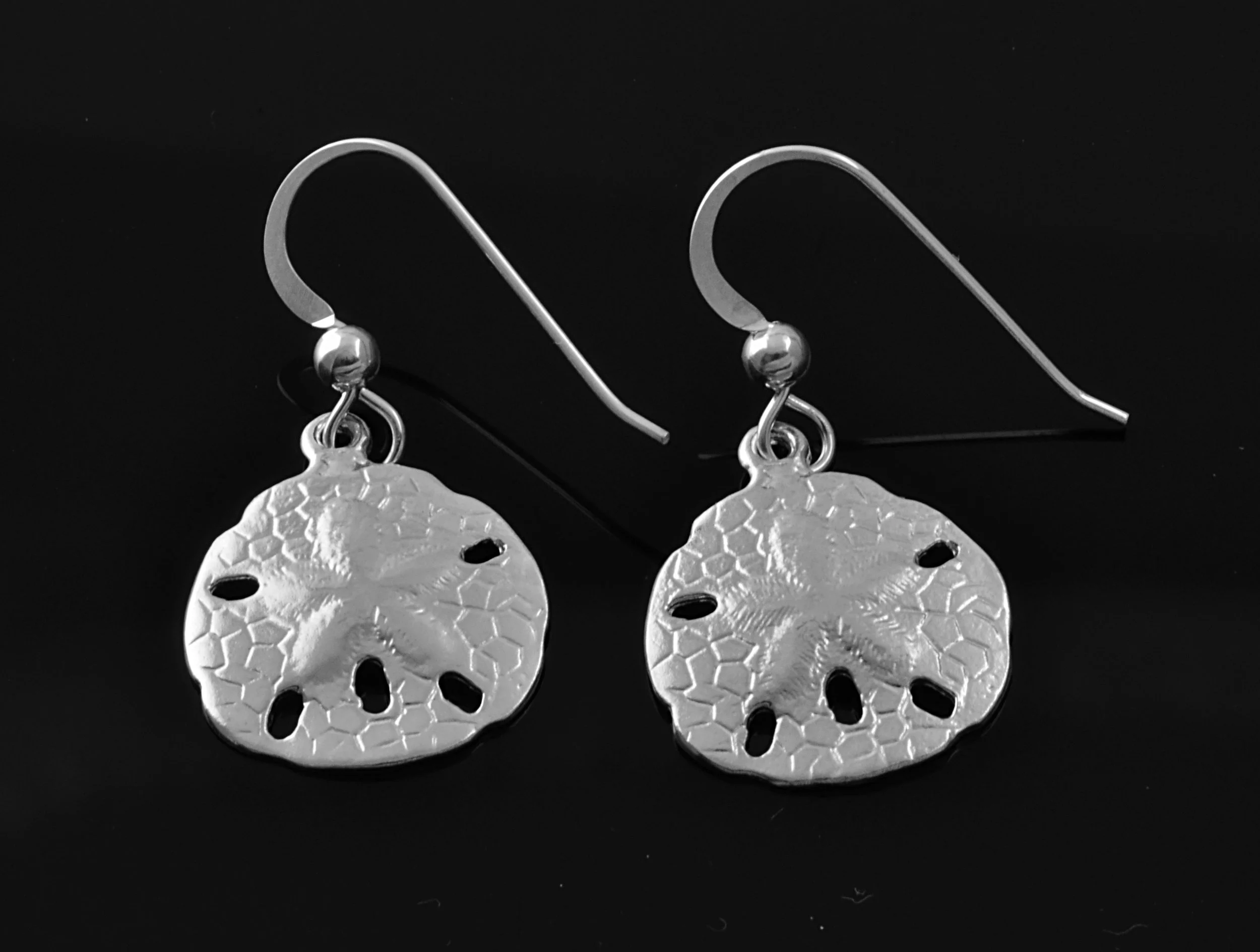 Medium sized sterling silver sand dollar wire earrings on a black background