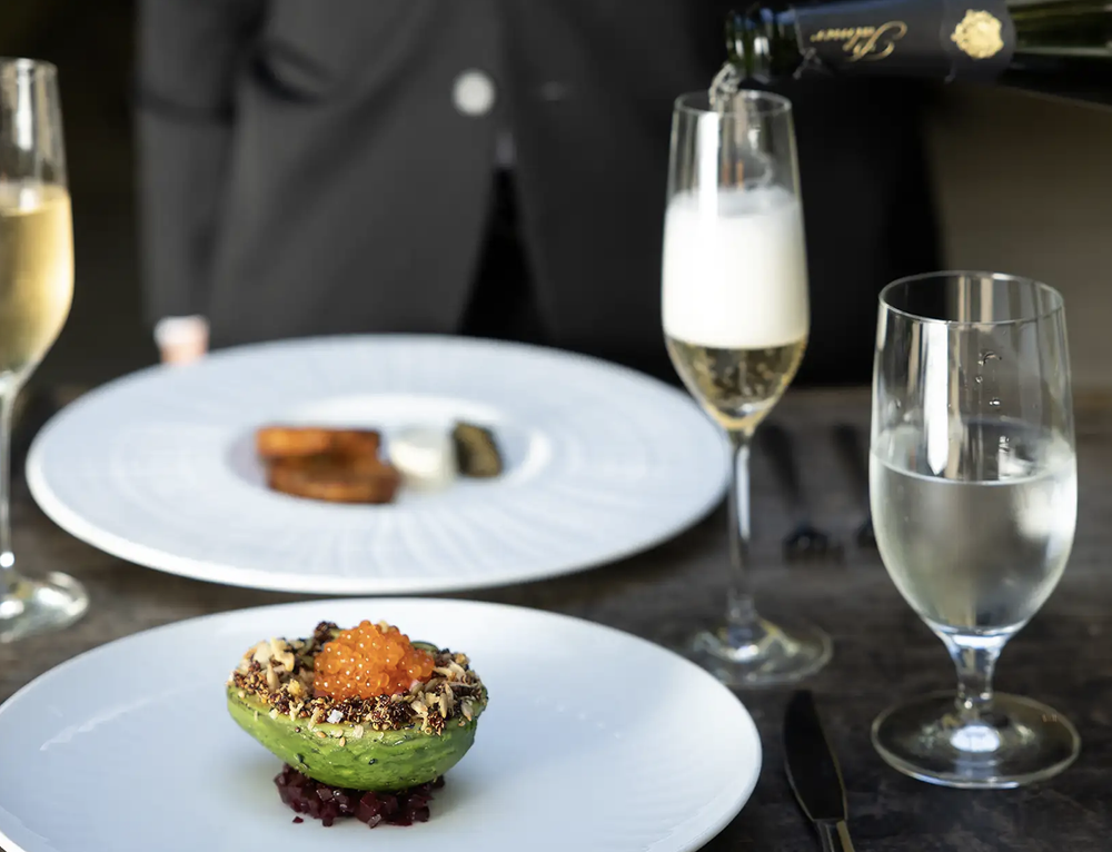 Avocado filled with roe and vegetables, served with champagne in an upscale dining setting.