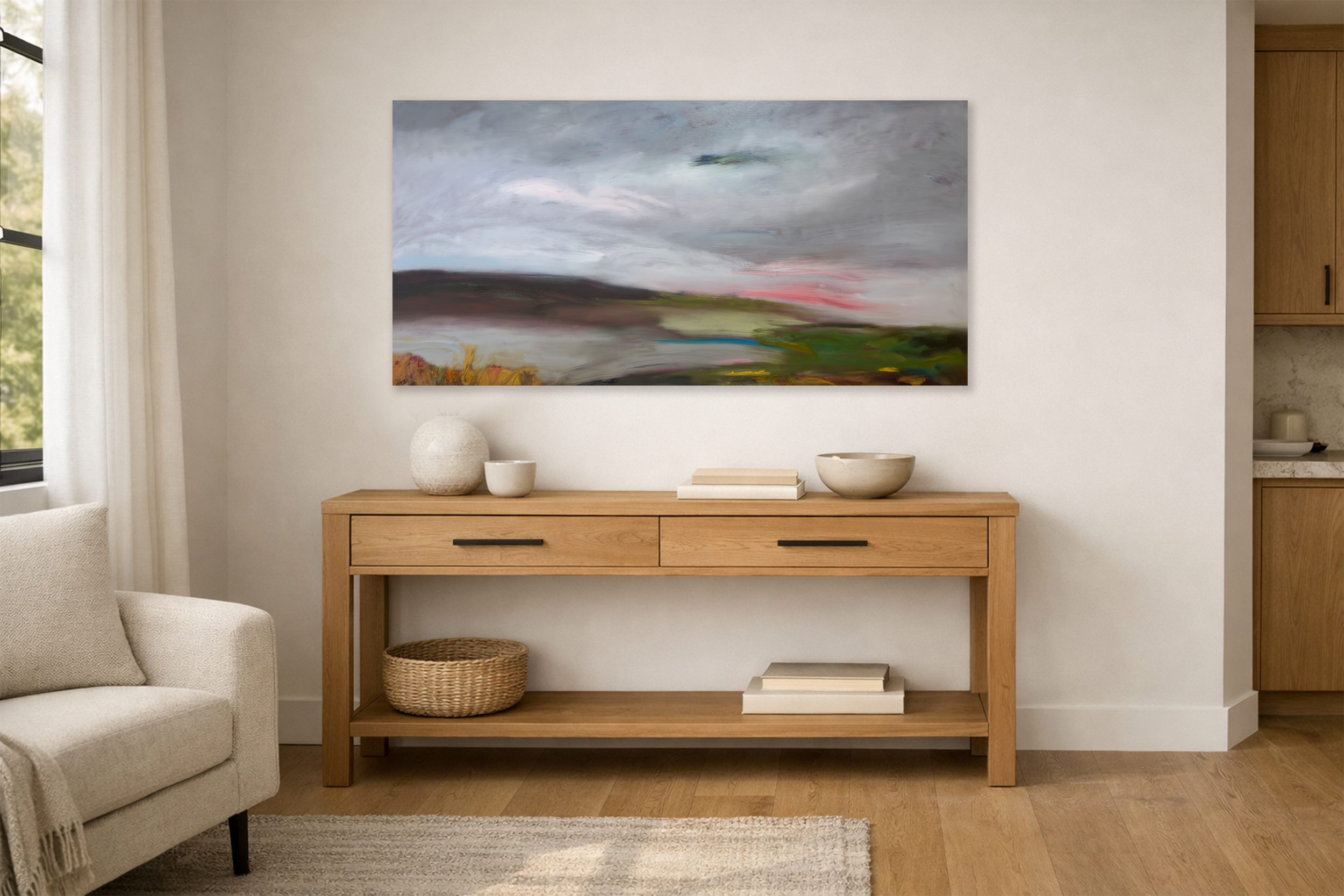 A large abstract landscape painting hangs above a light wood console table styled with ceramic objects, books, and a woven basket in a modern neutral living space.