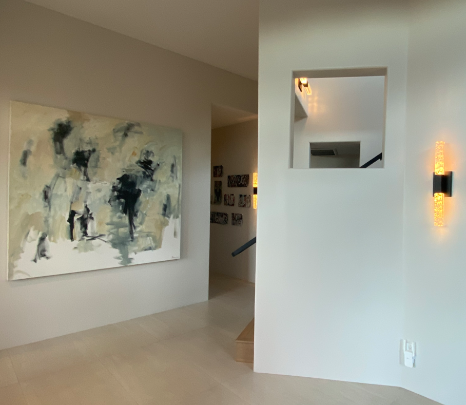 Modern interior with abstract and figurative paintings, warm wall sconces, and architectural hallway — showcasing contemporary art in a minimalist home.