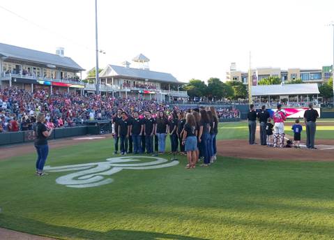 North Lamar High School Choir Director Rebecca Hildreth directs members of the Chamber Singers as they sing the national anthem before the first pitch of the Frisco Roughriders baseball game. 