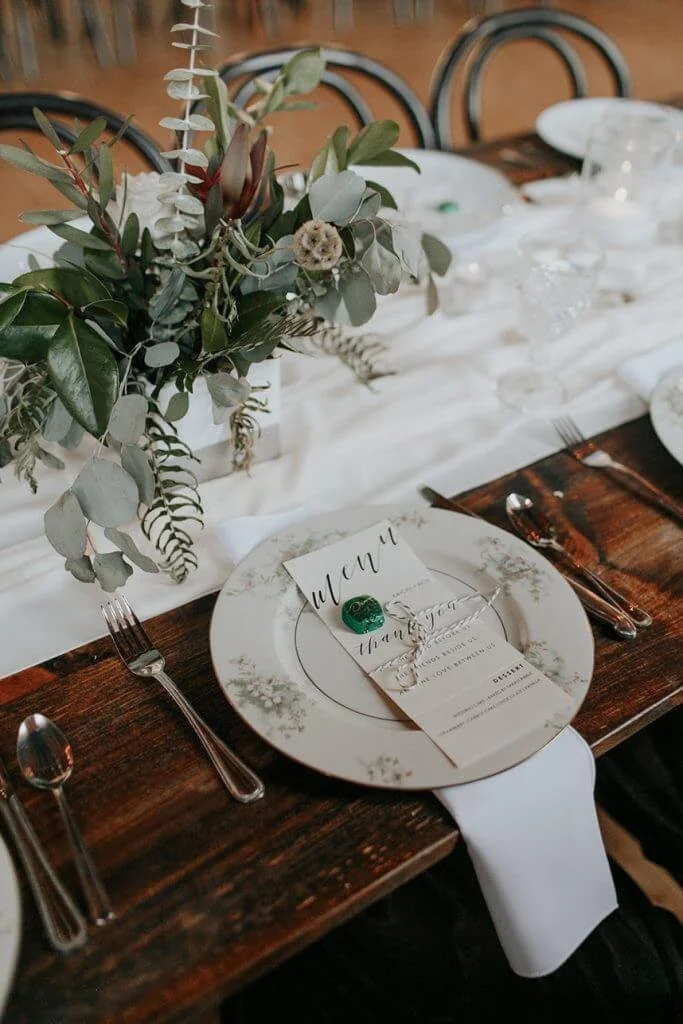 Event table detail with floral arrangement, printed menu, and place setting on a long wooden reception table