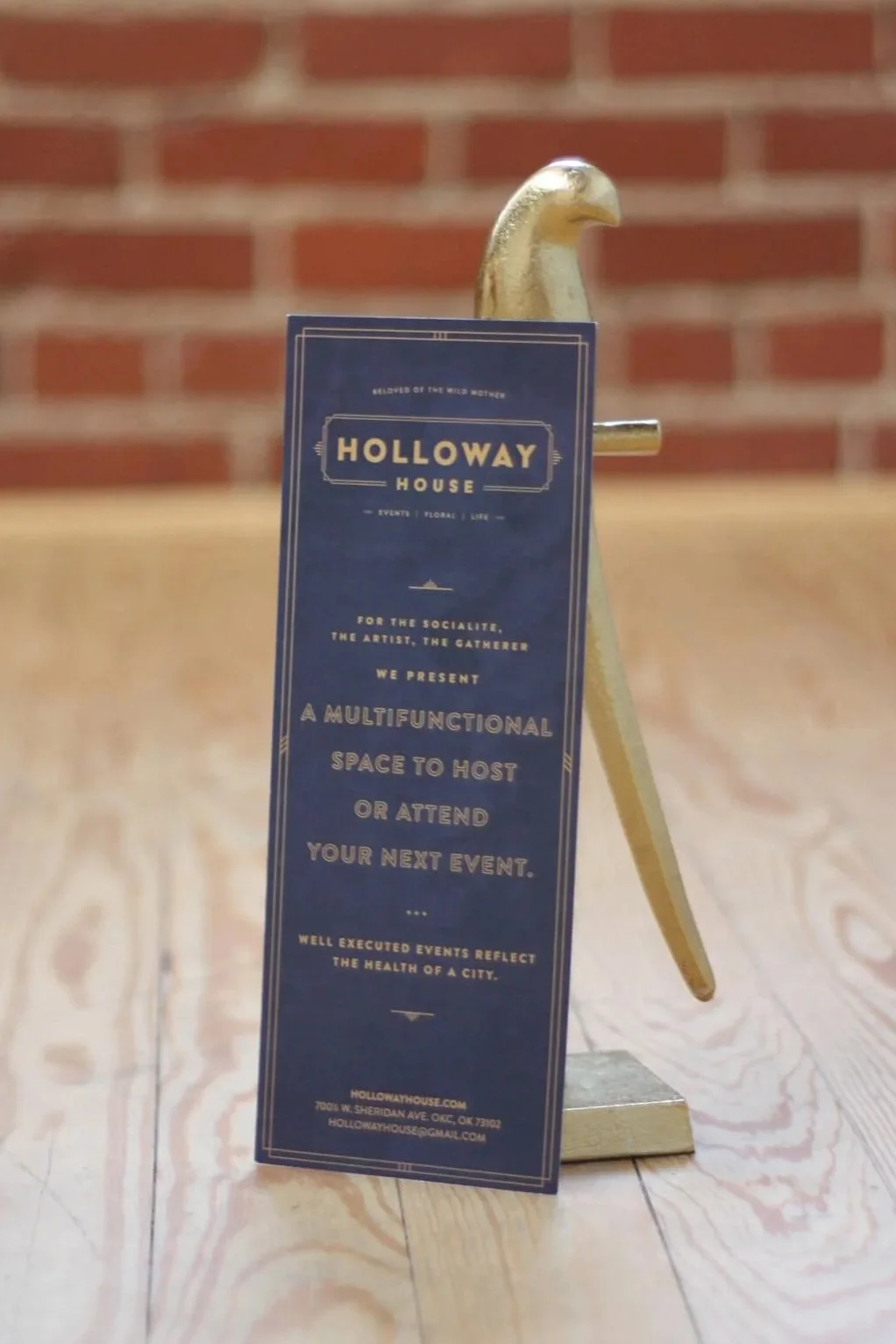Holloway House promotional brochure on a gold display stand in front of a brick wall.