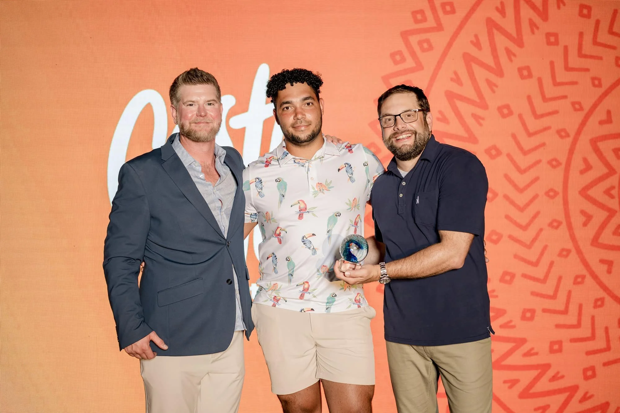 Three men standing in front of an orange backdrop at an awards ceremony