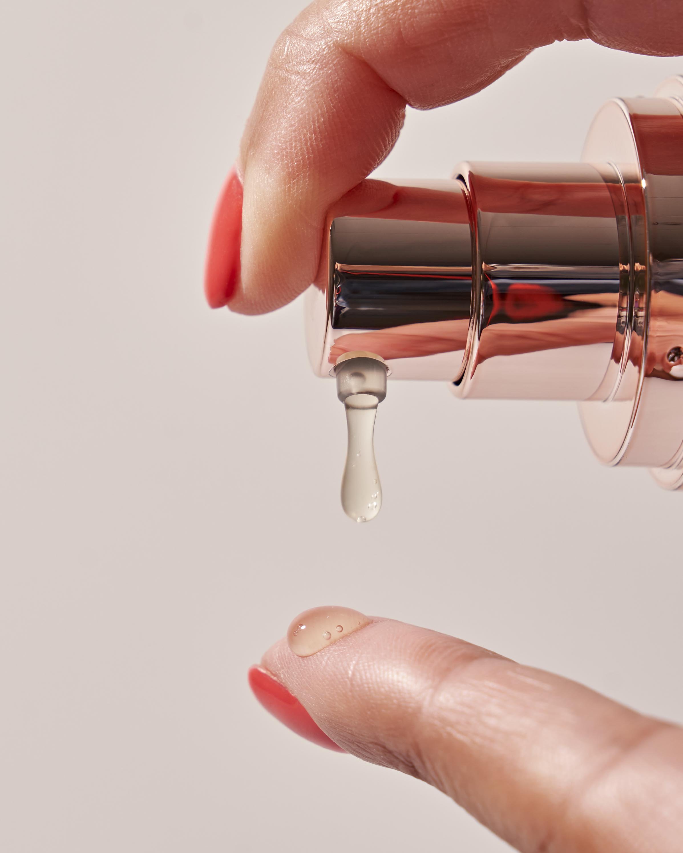 Close-up of a hand dispensing moisturizer from a rose gold pump bottle onto another finger.