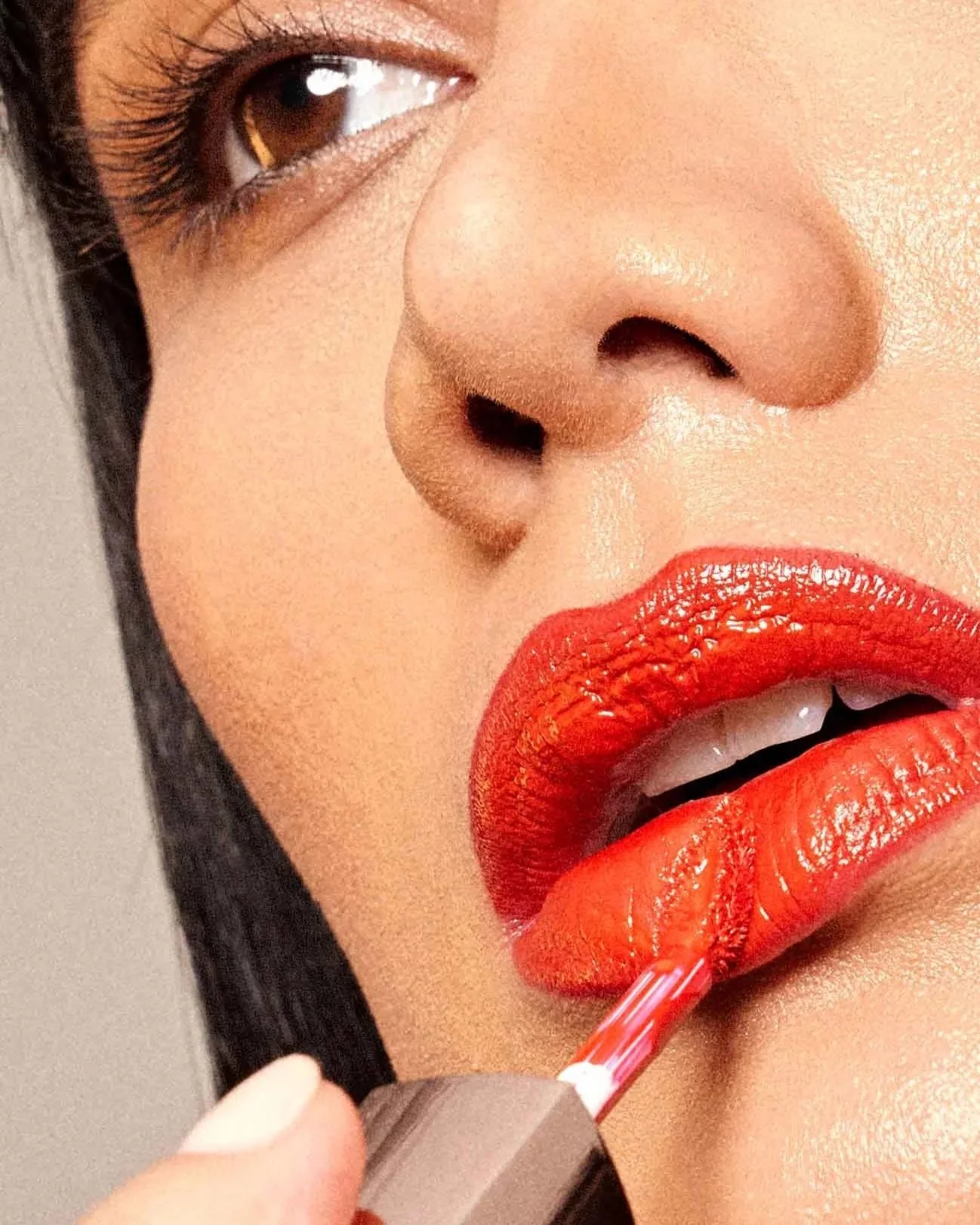 Close-up of a woman applying red lipstick with a lip gloss applicator.