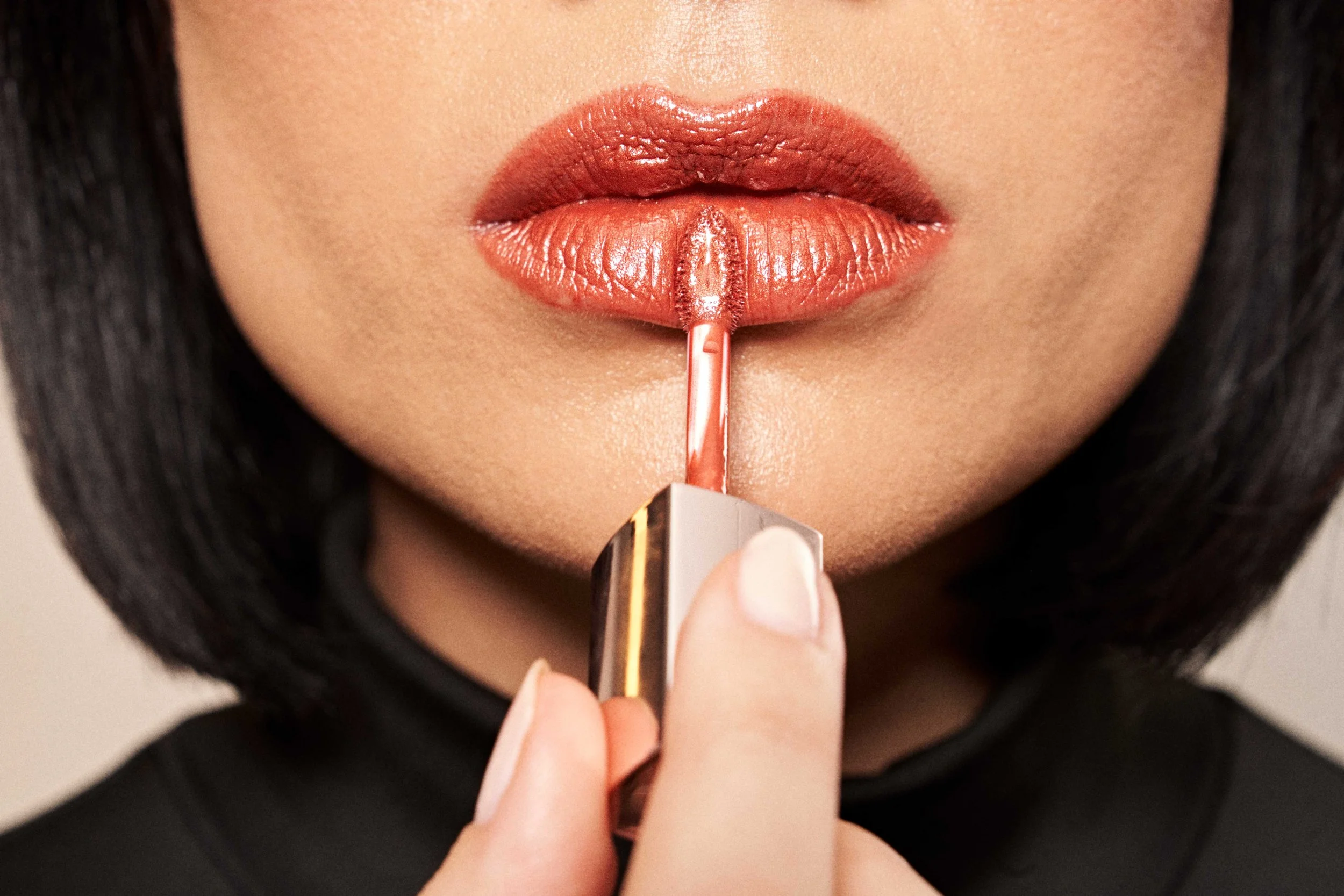 Close-up of a woman applying nude lipstick to her lips with a brush.
