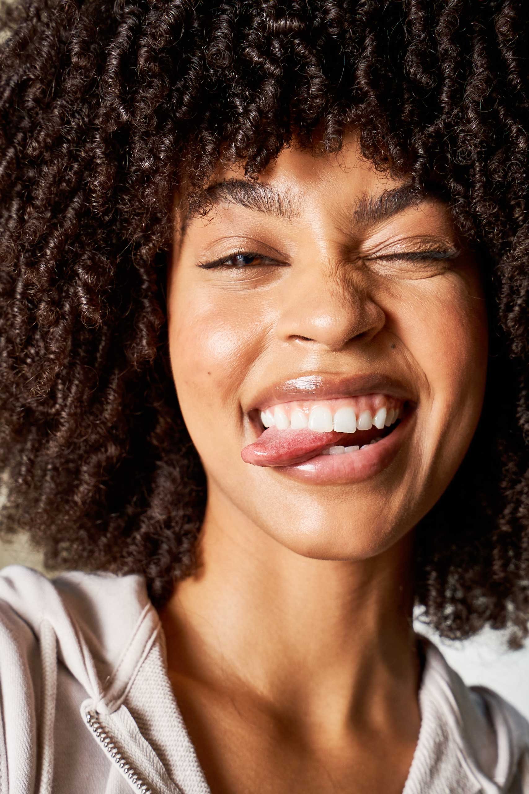 A woman with curly hair making a playful face, sticking out her tongue and winking.