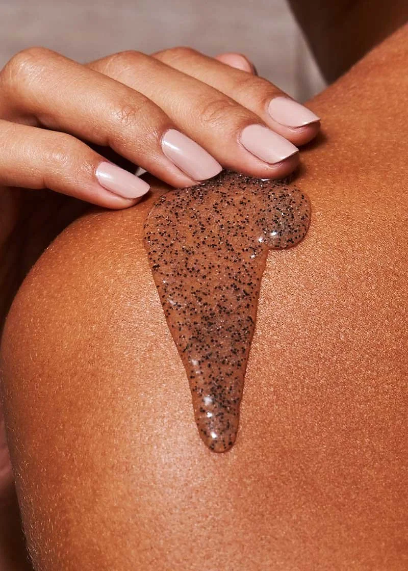 Close-up of a person's shoulder with glittery, brown body gel being applied with fingers.