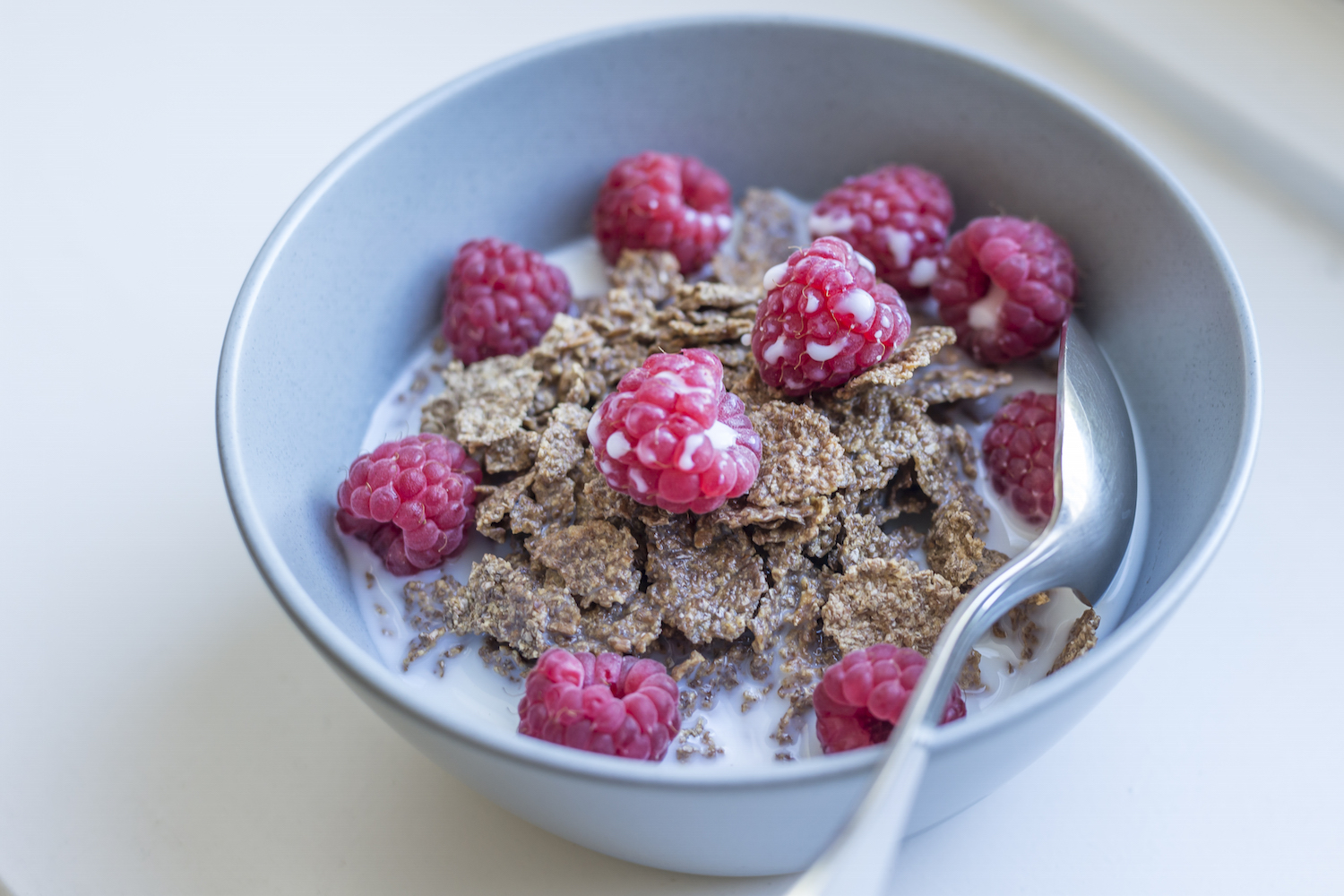 A bowl of bran flakes with fresh raspberries and milk.jpg