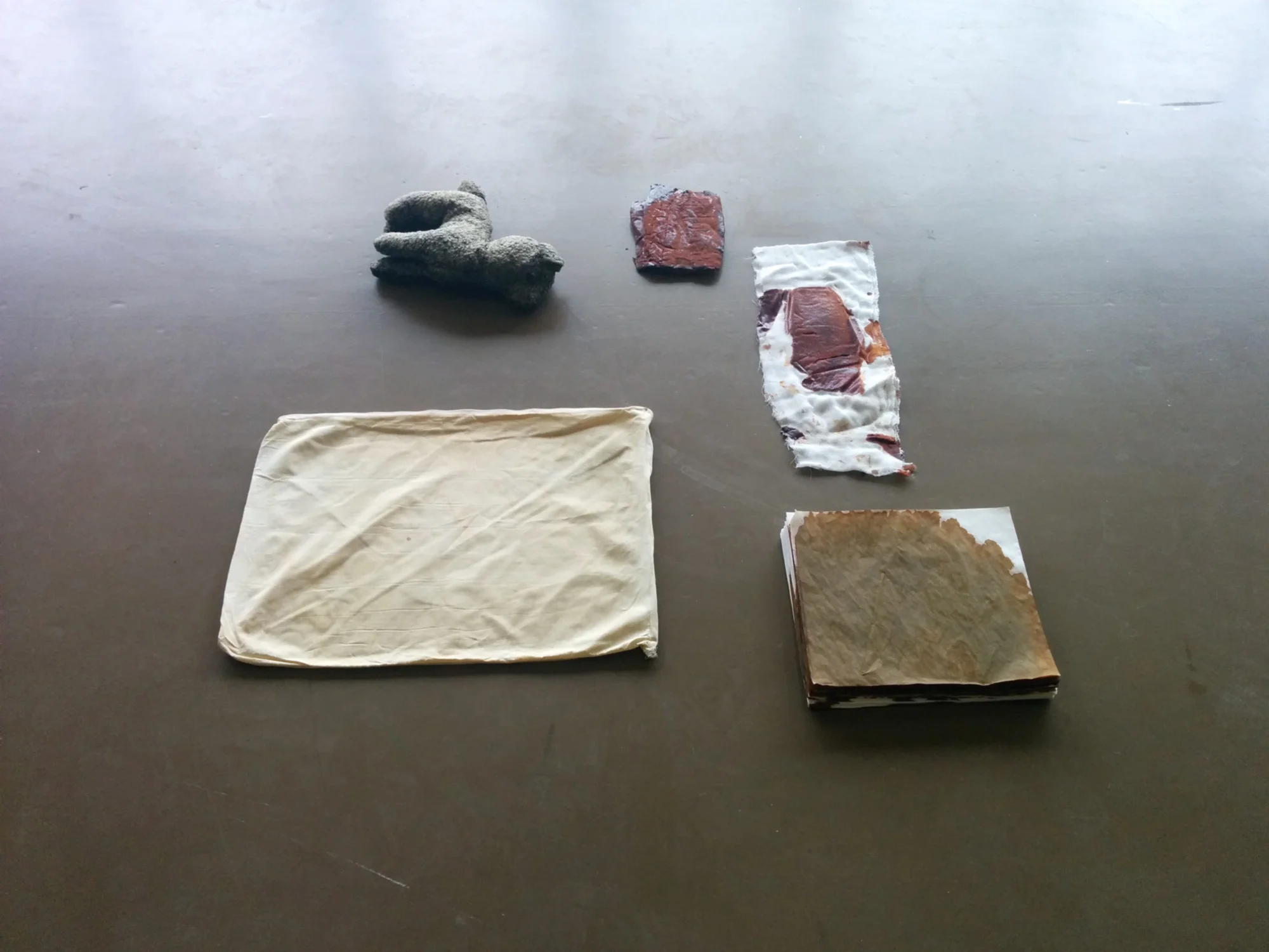 Soak (Everything=everything) , clockwise: 1. stuffed animal, 2.hardened betadine “stone” (gauze base), 3.betadine imprint on gauze, 4.poured betadine on stack of paper, 5.used pillowcase with light traces of mould and small bloodstain. Exhibition view “AIRE. Espaces intermédiaires”, Ancien Dexia Art Centre Vanderborght, March 2016.