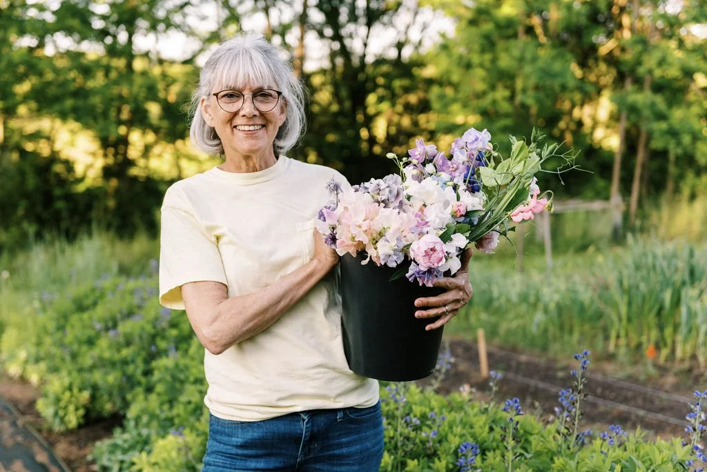 team member smiling holding a bucket of sweetpeas in the field