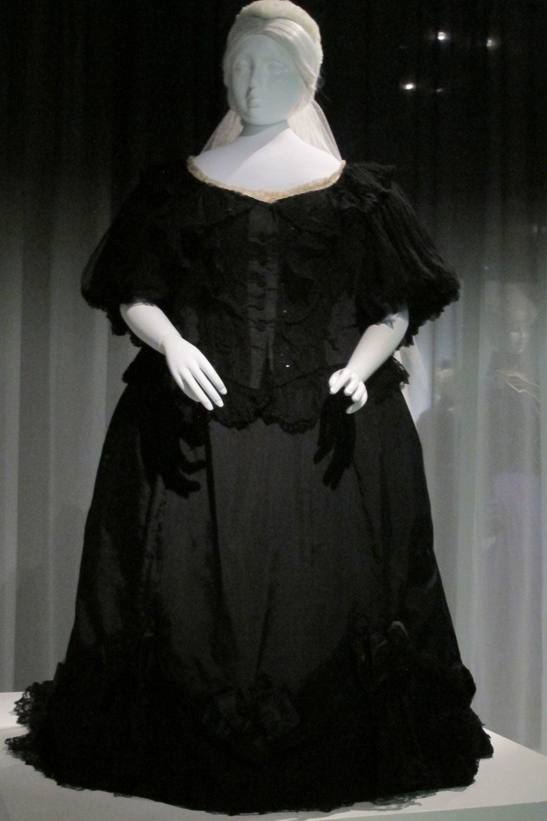 QUEEN VICTORIA MOURNING DRESS In black: silk taffeta, silk ribbon, silk lace, silk crepe, 1894-1895. The two views of Victoria’s dress show the magisterial sweep of her gown, as well as the dispensing of forms of corseting that would bind and reshape her fulsome figure. Brooklyn Museum Costume Collection at the Metropolitan Museum of Art.