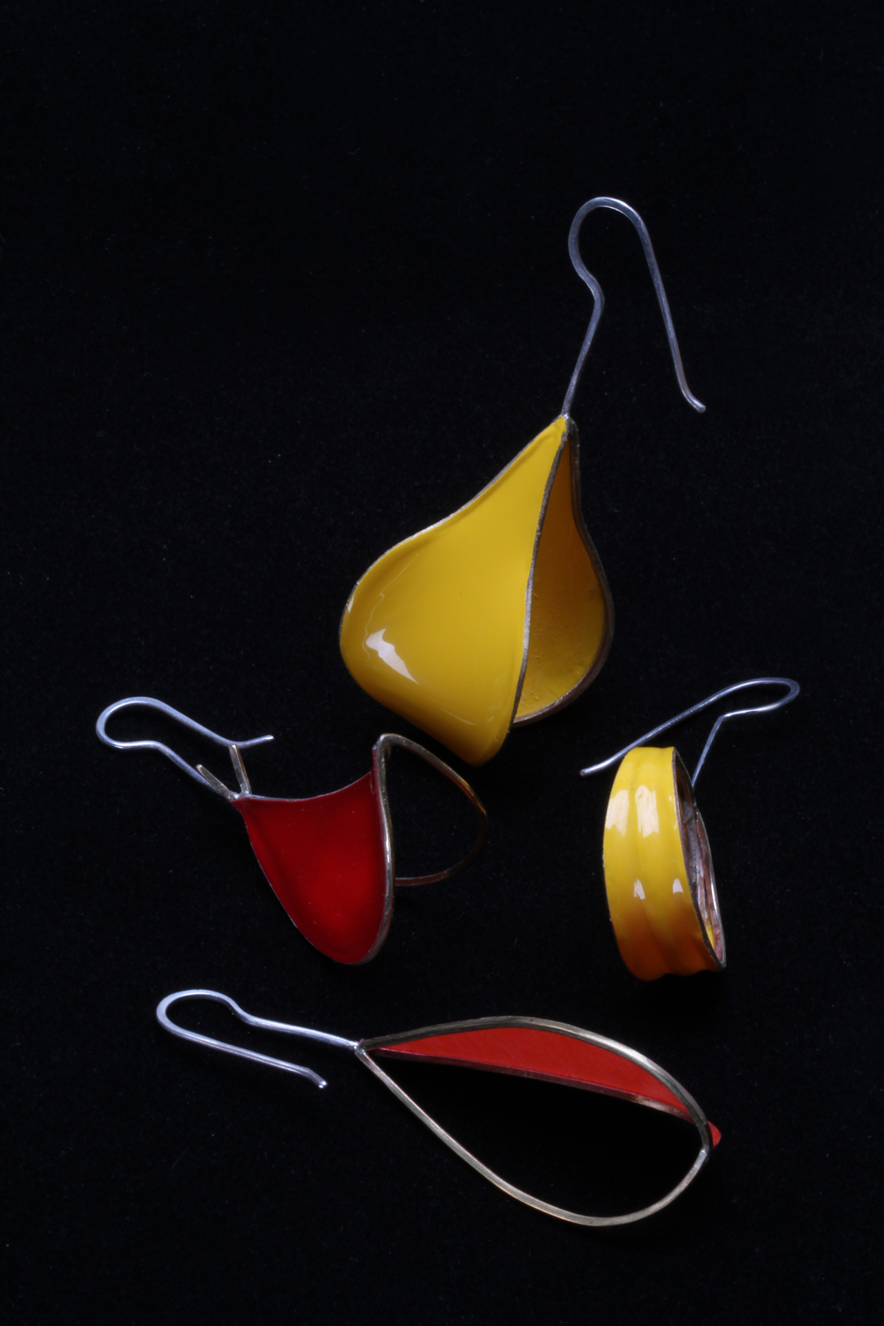 EARRINGS OF SQUARE BRASS AND ROUND STERLING SILVER WIRE, COVERED WITH COVERLITE OR ULTRACOTE COATINGS; both wires are 18 gauge. Brass square half-hard wire is formed on mandrels, while silver earwire are shaped with pliers and lightly forged. Except for the yellow triple coil earrings, all others have only one or two panels covered. Note that the top pear-shaped earring, covered with Ultracote, has really beautiful curved and complex surfaces caused by the heatshrinking of the model airplane coating. It is better shown in other photographs in next blog. Foreground Pod earring is ca. 7.0 cm long. All these photographs are taken with a Canon 7D, and 60 or 100mm Canon macro lens, and studio strobes, against Tufflock, transiluminated plex or Varitone backgrounds (Liu 2014b). Photographs by Robert K. Liu/Ornament.