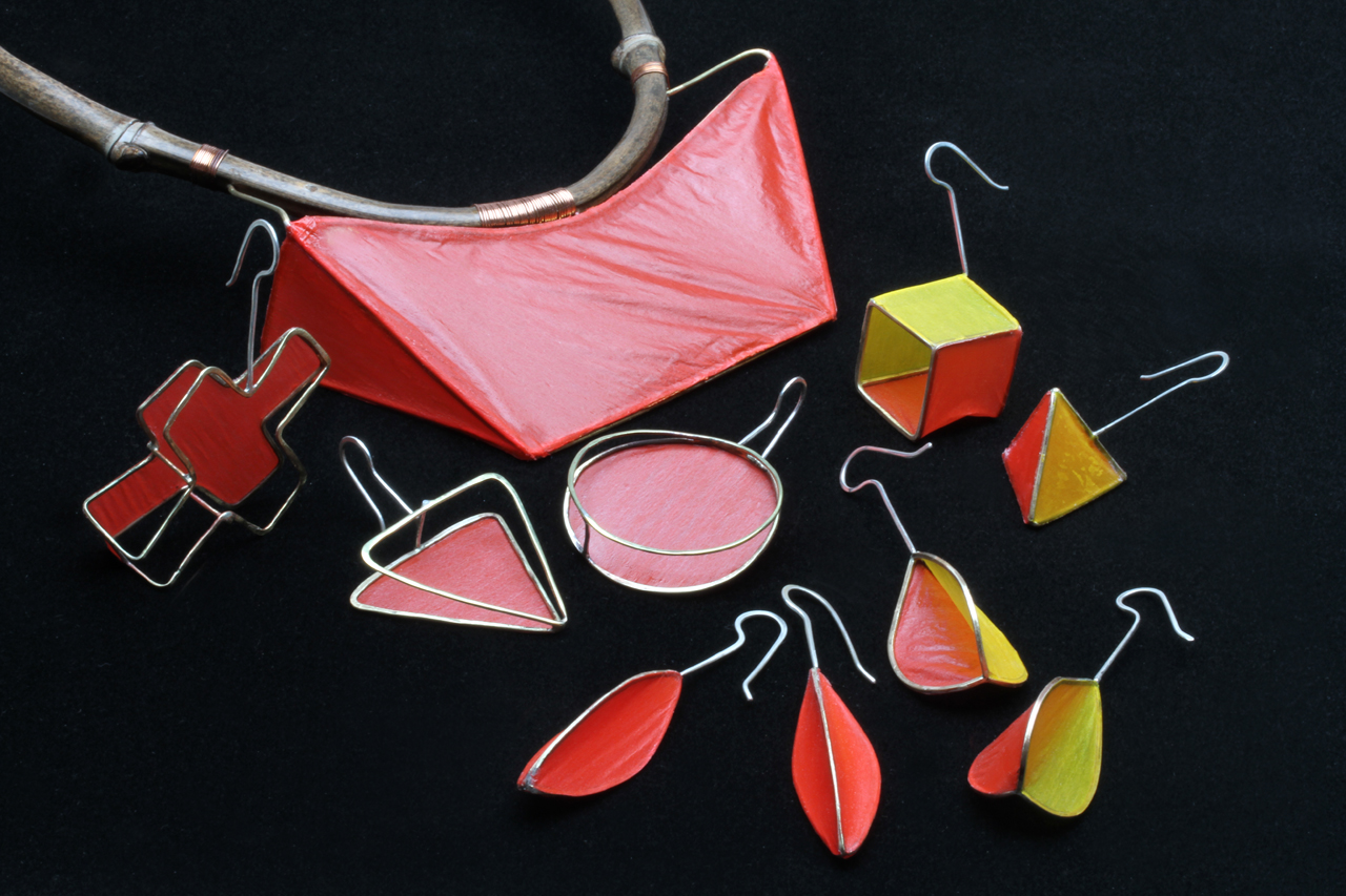 COVERLITE MATRIX PENDANT ON HEATBENT BAMBOO TORQUE AND WIRE MATRIX EARRINGS, some of which are in sets of three, to be worn in different asymmetrical pairs, or are an asymmetrical pair, like the yellow/red cube and triangle. In foreground are two pairs of symmetrical Pod earrings, with all red or red/yellow Coverlite skins. Earrings are 5.0-7.5 cm long and weigh between 1.6 to 3.1 grams each, all from 2014.