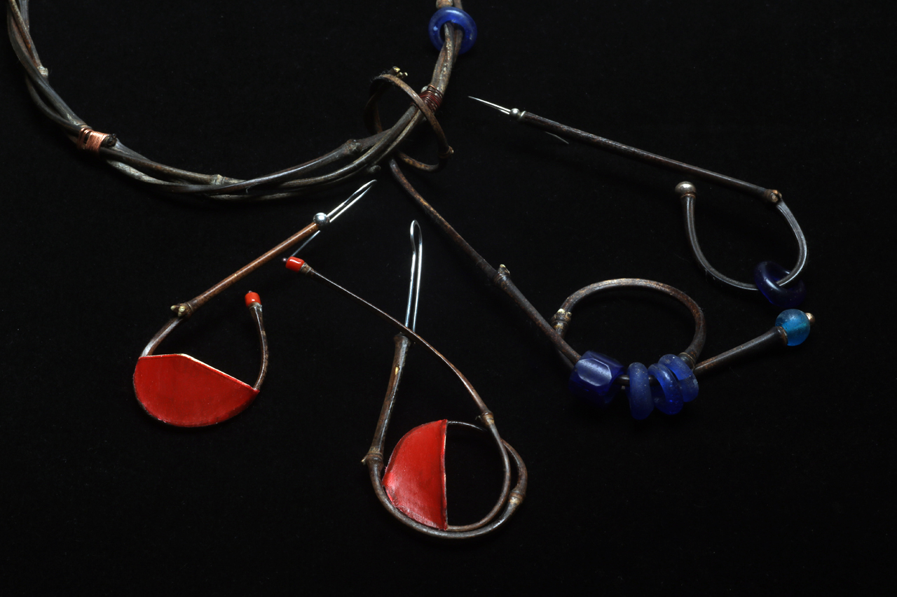 CLOSEUP OF TIGHT RADIUS BEND PENDANT, COMPARED TO SINGLE AND DOUBLE TIGHT RADIUS BEND EARRINGS; the one on the right is an older pair, made from bamboo harvested and dried for a long period, versus two Coverlite adorned ones on the left which are from freshly culled culms. The positioning of the wire matrix results in either horizontally or vertically oriented panels of red. Both have decorations of red precious coral and sterling silver beads, as well as hand-formed/forged silver earwires. The older example has vintage Bohemian glass, and Ethiopian silver beads for decorations. Earrings are 9.5 - 12.2 cm long.