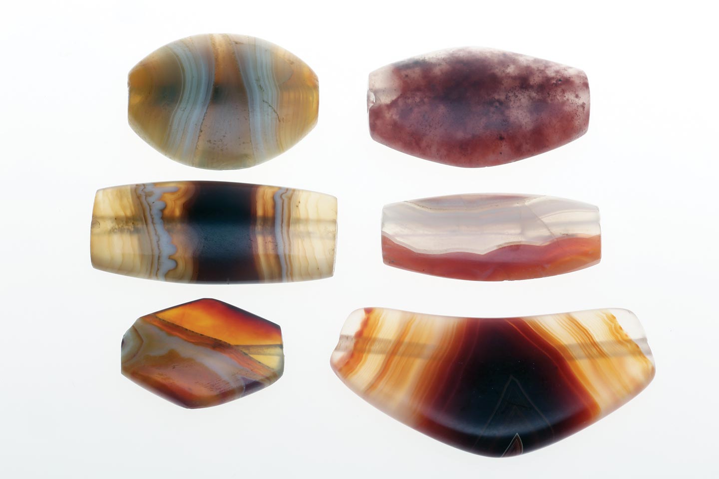 FOUR ANCIENT TABULAR/LENTICULAR HARD STONE BEADS FROM AFGHANISTAN AND TWO REPLICA AGATE BEADS; these carnelian and agate tabular beads are very similar to Mesopotamian third millennium beads, 2.8 - 3.5 centimeters long, 0.6 - 0.9 centimeters thick. Courtesy of Anahita Gallery and J. Lafortune, 1978. Two lowest beads are new replica tabular agate and leech beads from Iran and Cambay, 0.6 - 1.0 centimeters thick; Courtesy of W. Seifried, 2006 and Beadazzled/Kamol, 1999. Due to better lapidary equipment, especially drills, many replica beads are now thinner than the prototypes. Photographs by Robert K. Liu/ Ornament ; shot with studio strobes, using softboxes for both transillumination/reflected lighting or just reflective lighting when shooting on black Tufflock. 