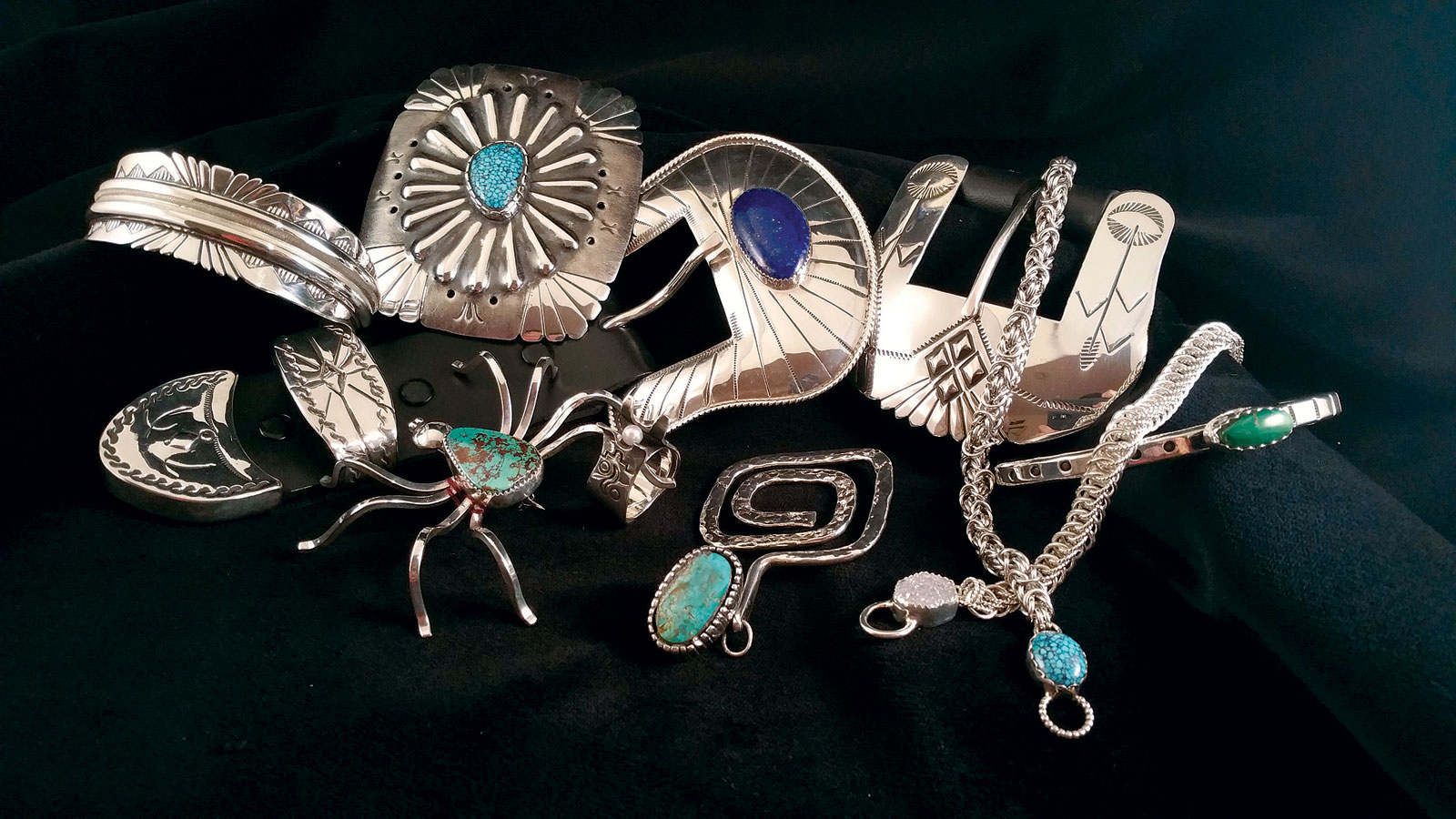 JEWELRY BY JERRY E. GAUSSOIN JR. (left to right, top to bottom) : Navajo Mother Earth bracelet, 2017; Navajo Four Cardinal Directions concho style buckle, 2017; Ranger belt buckle, 2015; Simplicity cuff, 2017; Navajo Spider brooch, 2014; Pueblo Protector ring, 2017; Pueblo Maiden pendant, 2017; Byzantine Chain bracelet, 2017; and Half Persian chain bracelet, 2017. All jewelry is fabricated, some hand-stamped, formed and/or textured, set with turquoise or lapis. Photograph by Jerry E. Gaussoin Jr.
