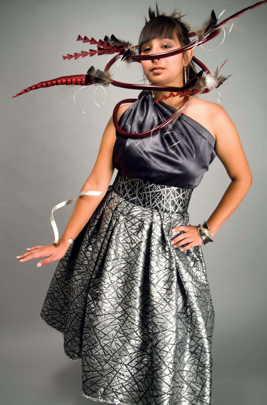 POSTMODERN BOA, collaboration by David Gaussoin and Wayne Nez Gaussoin of stainless steel, sterling silver, enamel, paint, and feathers, 2009. TEARDROP EARRINGS by David Gaussoin of sterling silver, 8.0 centimeters long, 2009. EFFUSION BRACELET by Wayne Nez Gaussoin of sterling silver, 30.5 centimeters long, 2009. GLISSADE BRACELET by Wayne Nez Gaussoin of sterling silver, stainless steel, 15.2 centimeters diameter, 2009. DRESS by David Gaussoin and Tazbah Gaussoin of metallic blended material and silk, 2009. Photograph by Museum of Indian Arts and Culture. Model: Tazbah Gaussoin.