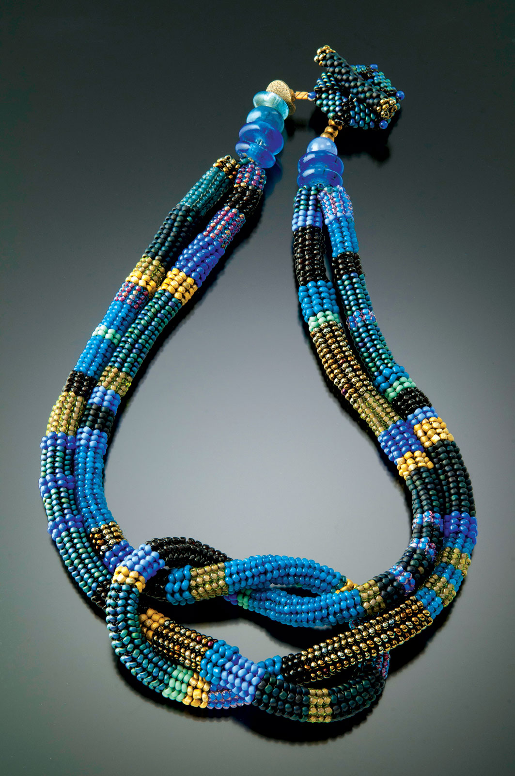 WISTERIA AND LEAF SQUARE KNOT NECKLACE of glass beads, woven in a spiral herringbone stitch with a needle and fishing line. The hollow tube is filled with small glass beads and then knotted into a square knot form; with recycled glass, stone beads and handwoven toggle closure, 45 centimeters long x 5 centimeters high, 2014. 