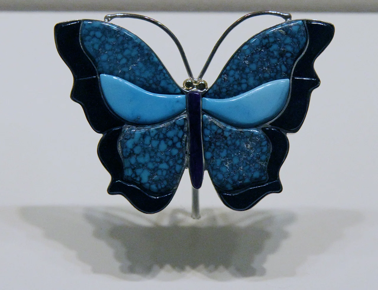A butterfly with turquoise wings, most likely also made by Liz Wallace, but I cannot be sure. Again, the shadows cast by the exhibition lighting adds to interest.