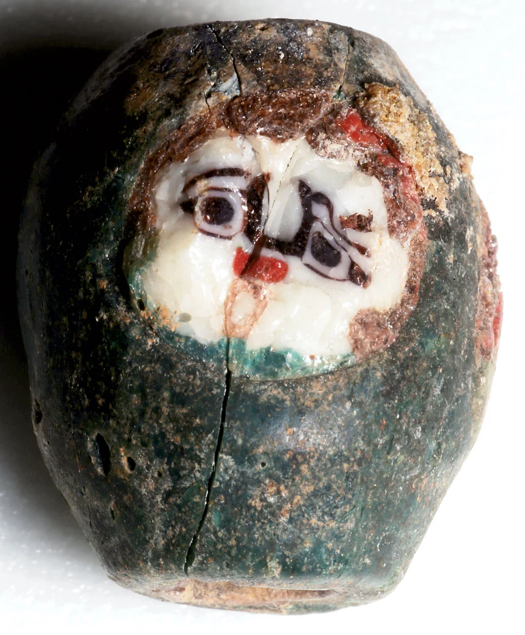 GREEN BARREL BEAD WITH TWO FACES, found in Nubia; faces appear to be a version of Gorgon, but not seen before. Brown glass may denote hair. The face cane shown is battered and of very white glass. This bead (21.12473.4) was found with the eyebeads with gold foil or bands on the last page. Courtesy of the Museum of Fine Arts, Boston.