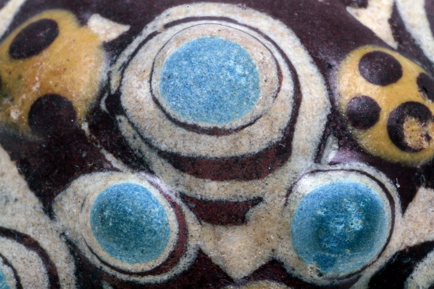 EXTREME CLOSEUP OF WARRING STATES COMPOSITE BEAD, of low-fired glaze over faience core of plant ashes. The image spans a width of 1.6 centimeters of the 2.9 centimeter diameter bead. This bead is virtually the same as an approximately fifth century B.C. specimen analyzed by Wood et al . (1999). Their bead had the same makeup and colors, which are common to many composite beads. While it is not clear how the low-fired glazes are applied, one can see from this closeup that some are precisely brushed on (?), others appear to be dabbed on in layers, eventually resulting in stratified or mounded/rounded eyes or rosettes, probably due to the high surface tension of the glazes or the glazes incompletely melting (Wood 2001). Shot with 100mm macro, 36mm extension lens, ISO 100 and studio strobe.