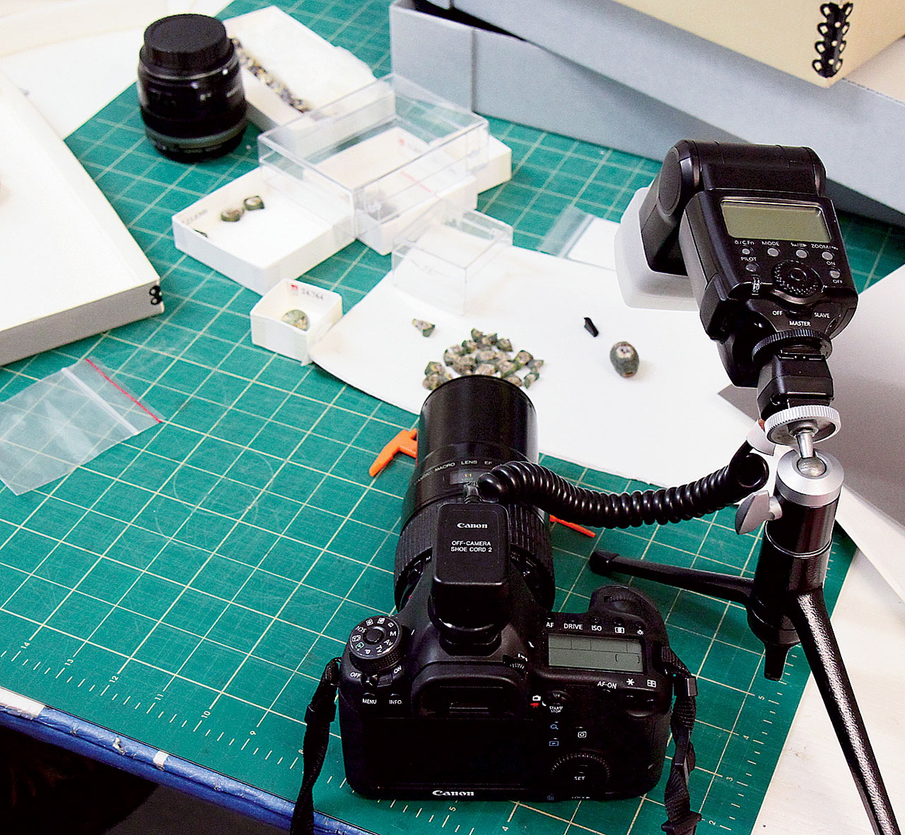 PHOTO SETUP AT BOSTON MUSEUM OF FINE ARTS FOR SHOOTING NUBIAN GLASS FACE BEADS, with Canon 7D, 100mm macro and 12mm Kenko extension ring. Camera is coupled with cable to Canon Speedlite 580EX, with plastic diffuser, that is mounted on a Leica ballhead and table tripod. Camera was handheld, with the tripod mounted light source aimed at glass face beads on white background paper (Liu et al . 2017).