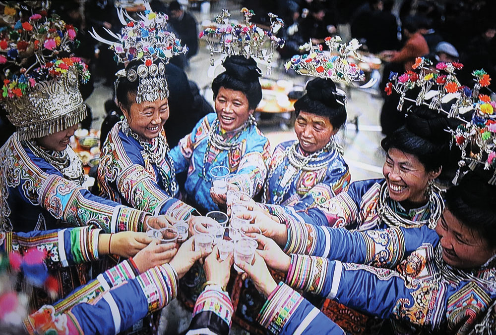 MIAO WOMEN enjoying a New Year celebration, part of a slide show in the “Vanishing Traditions” installation. They are likely saluting each other with baijiu , a noted clear liquor.