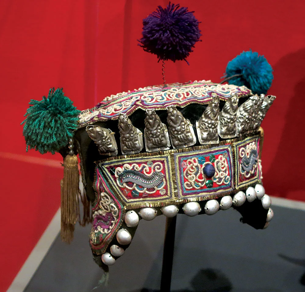 DONG CHILD’S HAT, decorated with pompoms and the eight Daoist immortals, of cotton, silk, silver alloy, embroidered, Liping or Rongjiang County, Guizhou Province, China, mid-twentieth century. Photograph by Patrick R. Benesh-Liu .