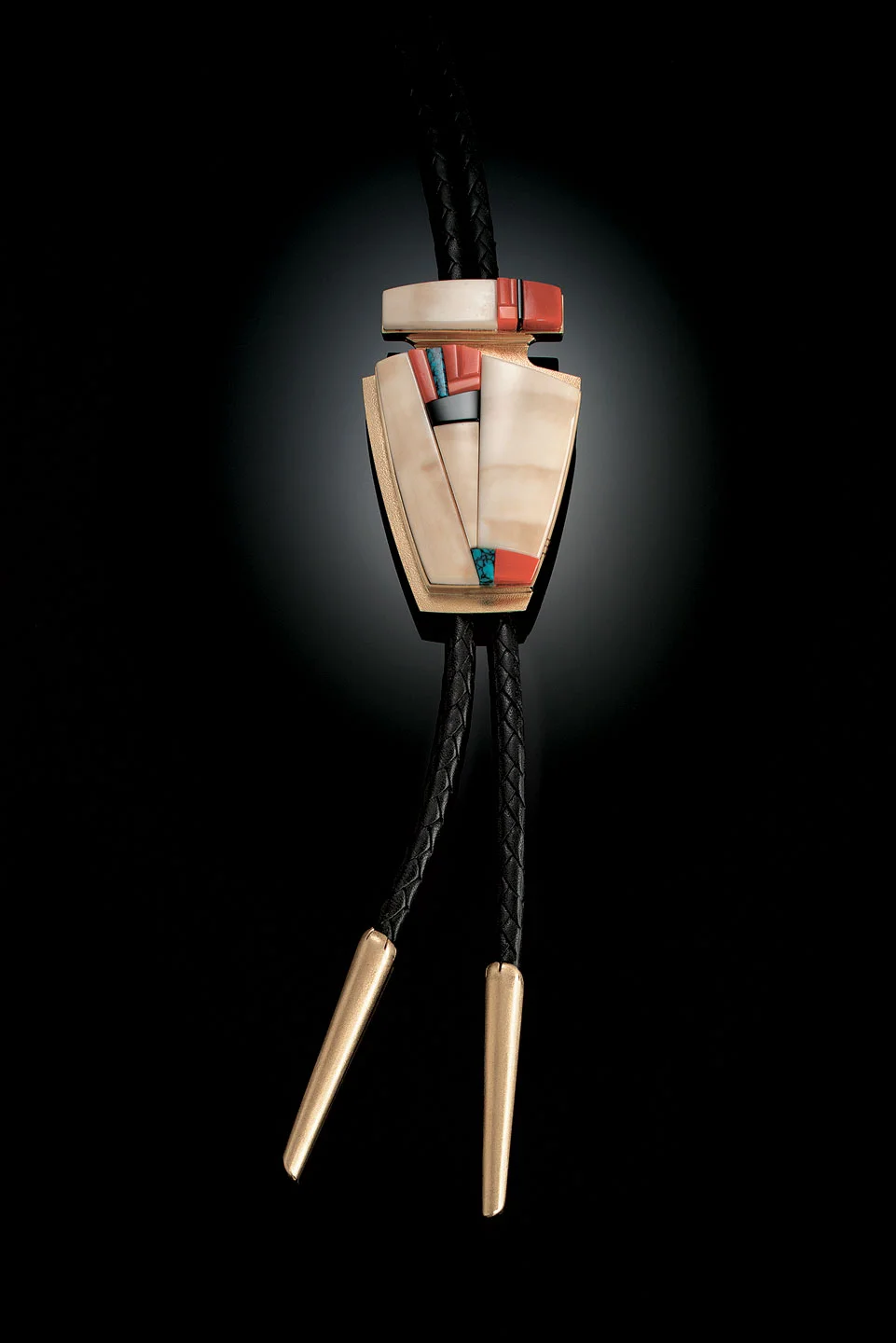 BOLO TIE of fossilized ivory, coral, black jade, turquoise, and fourteen karat gold, 8.3 x 5.4 centimeters, 1998. Private Collection.