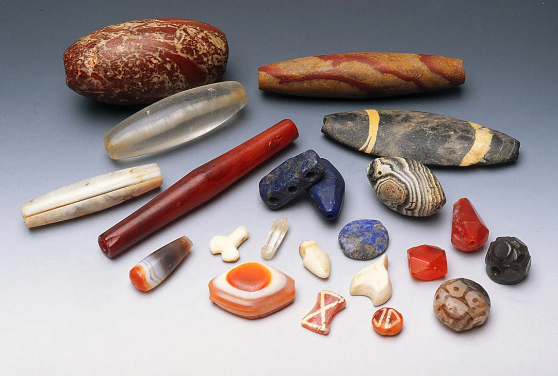 Assortment of ancient stone and shell beads from Afghanistan, including etched beads, agate and carnelian. Note lapis beads, including spacer, very clear quartz crystal bead showing perforation and quartz crystal, pierced at top as pendant. RKL