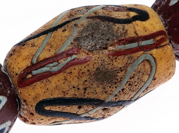An akoso powder glass bead, with a worn surface, so that the gray glass core shows partially; it is decorated with preformed glass threads. See Ornament issue 25 (2), Winter 2001, still available as a printed copy or pdf for detailed information on African powder-glass beads. RKL