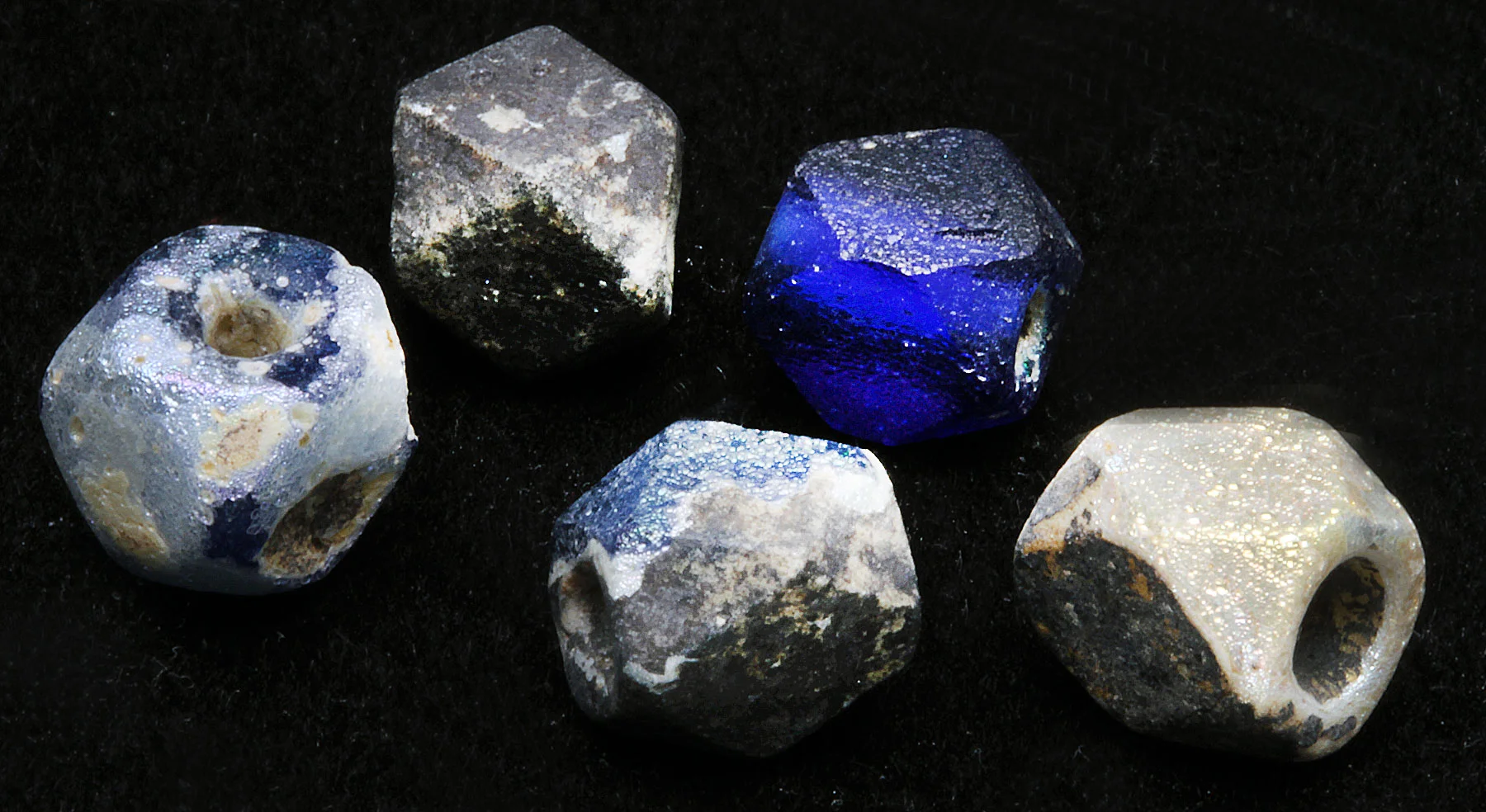 Roman period cornerless glass beads with varying degrees of iridescence, or weathering. It is likely these small drawn beads were made into cornerless cubes by facetting, and not marvering. These are 0.7 to 0.8 cm diameters. RKL