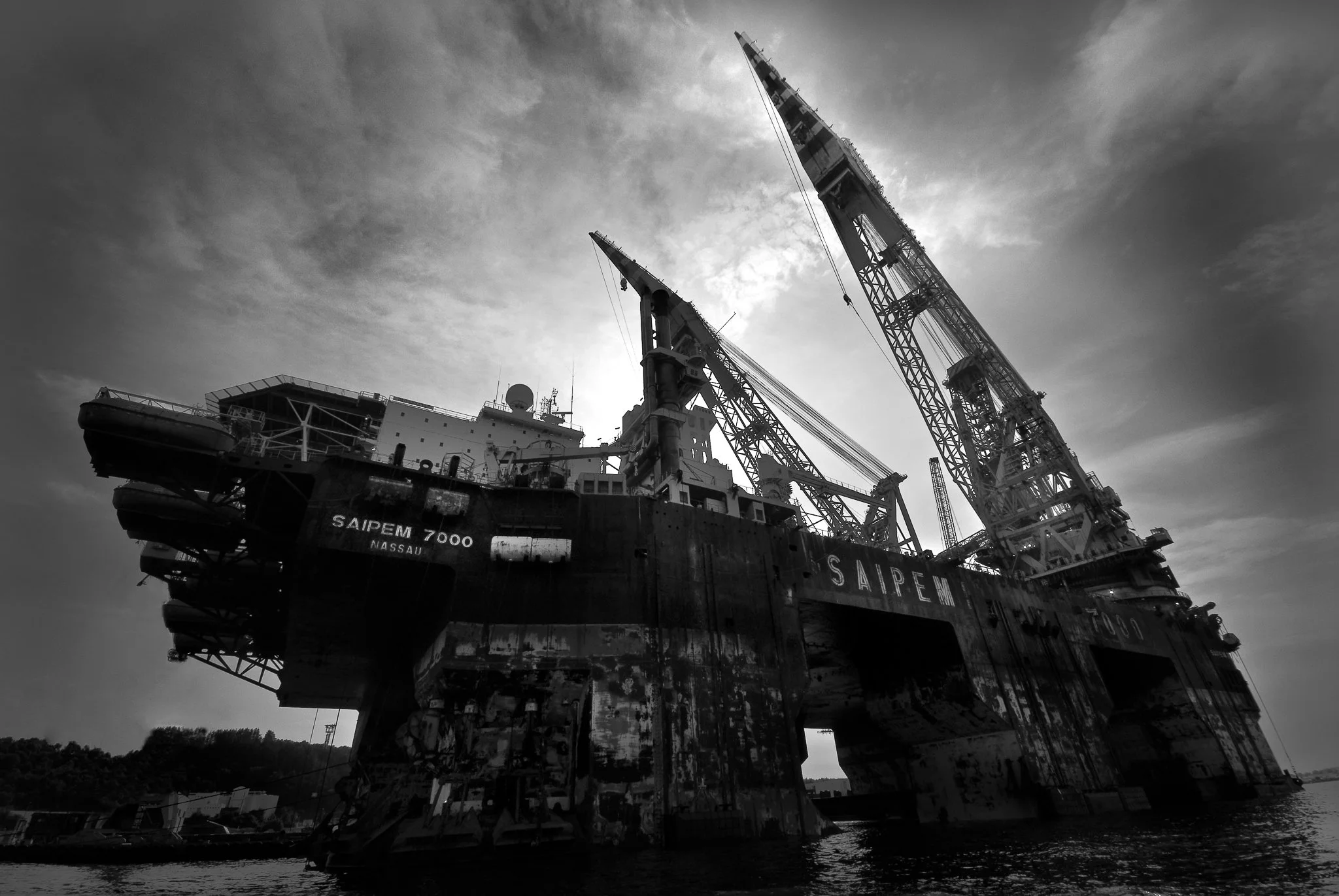 Utsikt over en havn med kraner og et stort fartøy ved kaia, med bybygg og fjell i bakgrunnen.
