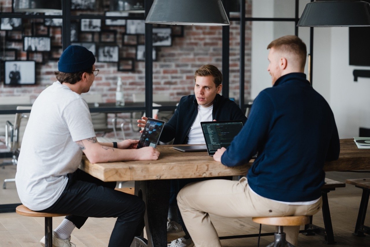  3 startup gründer sitzen an einem massiven holztisch und machen ein brainstorming 