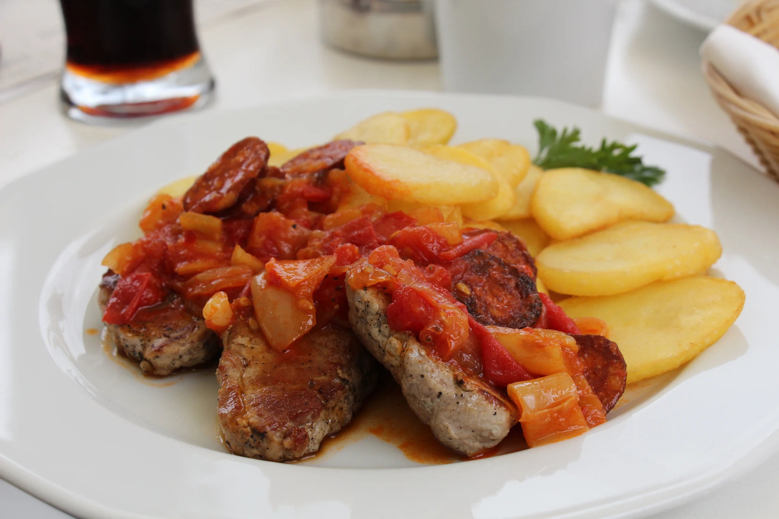 Grilled meat covered in tomato and onion sauce with slices of sausages