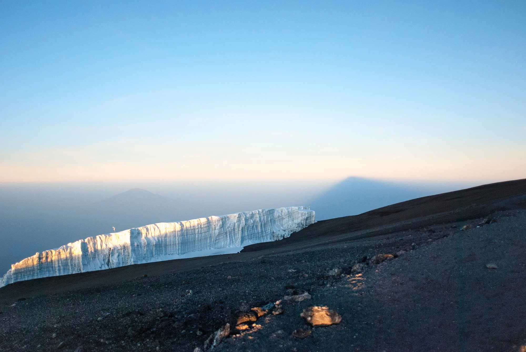 Mount Meru peeks above the glacier. To the right, the shadow of Kibo, Kilimanjaro's tallest peak, stretches to the horizon.