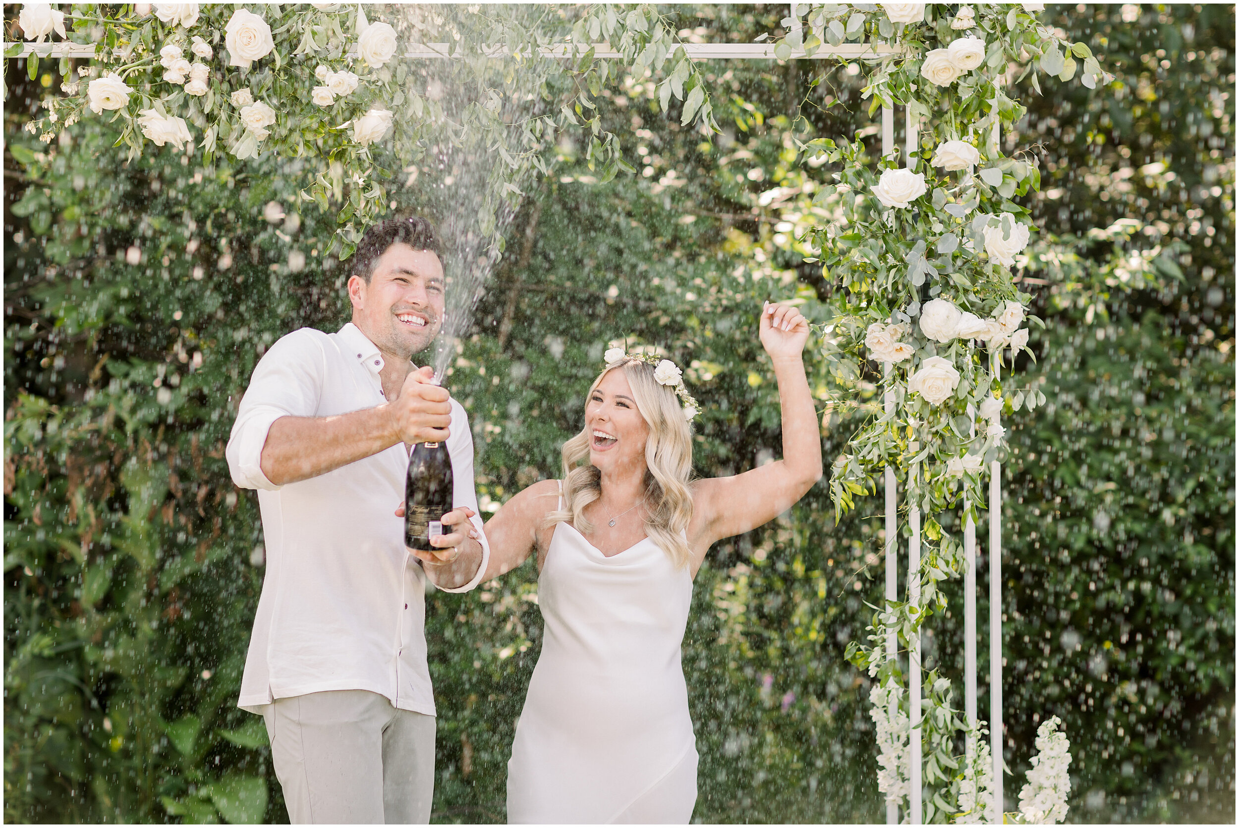  Beautiful bride and groom spraying champagne during wedding ceremony at outdoor backyard wedding in Ottawa, ON by Chelsea Mason. boho outdoor backyard wedding champagne at wedding spraying champagne at wedding outdoor wedding ceremony flower arch we
