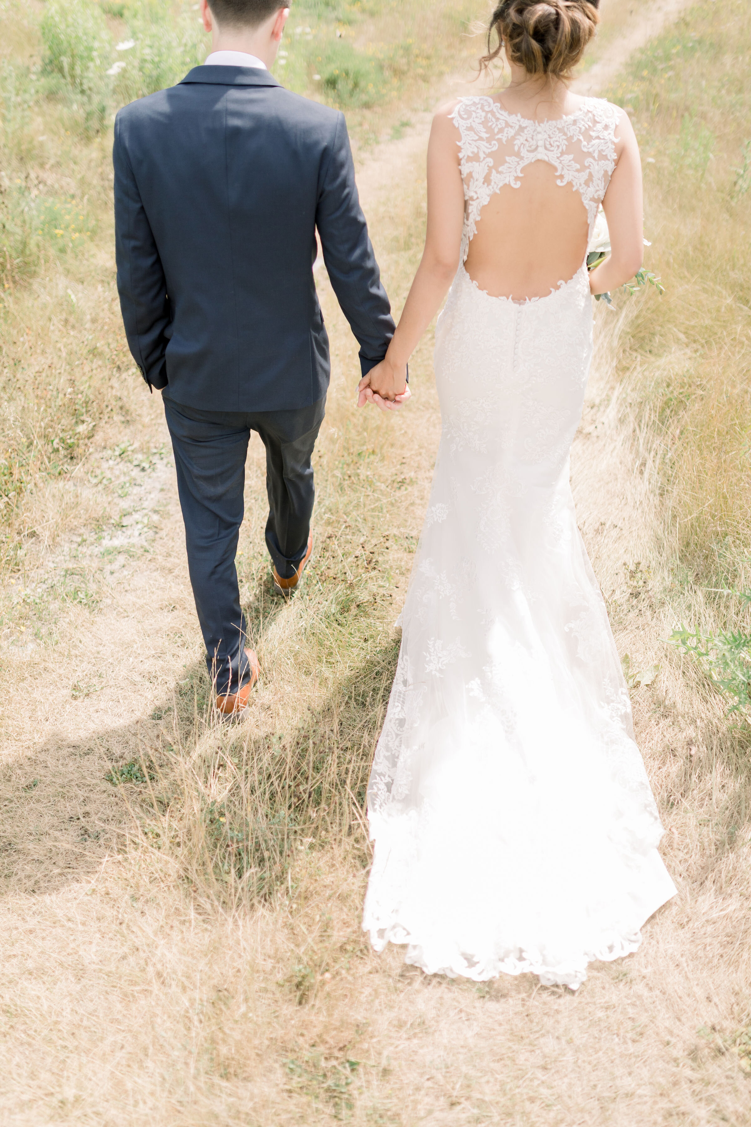  Bride in open back wedding dress with oval lace and long lace train and groom in blue suit by Chelsea Mason Photography in Ottawa, ON. backless wedding dresses open back wedding dresses lace wedding dress lace wedding train hair inspo for wedding na