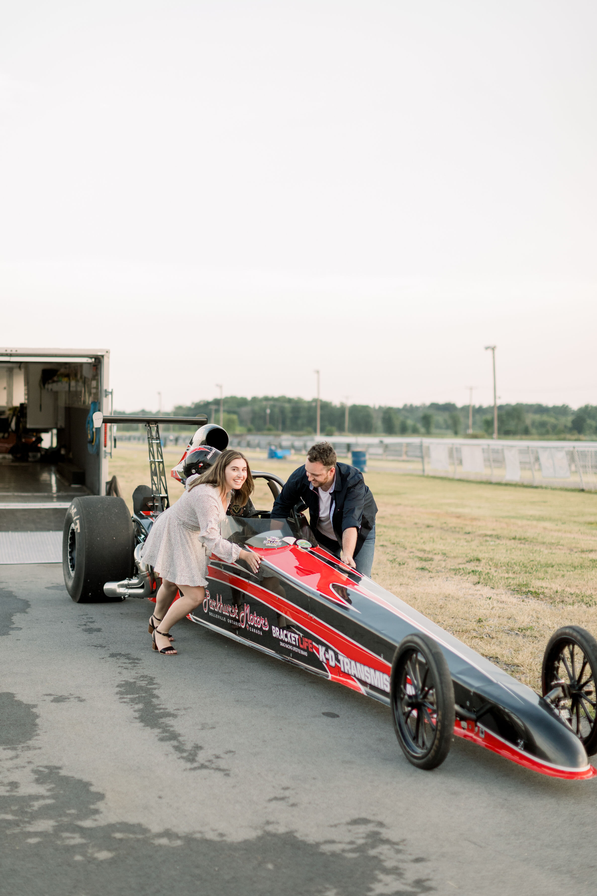  Beautiful couple in engagement photo session with racecar at a racetrack in Ottawa, ON by Chelsea Morgan Photography. cars in engagement photoshoot race track location for photoshoot outdoor engagement location in ottawa best photographer in ottawa 