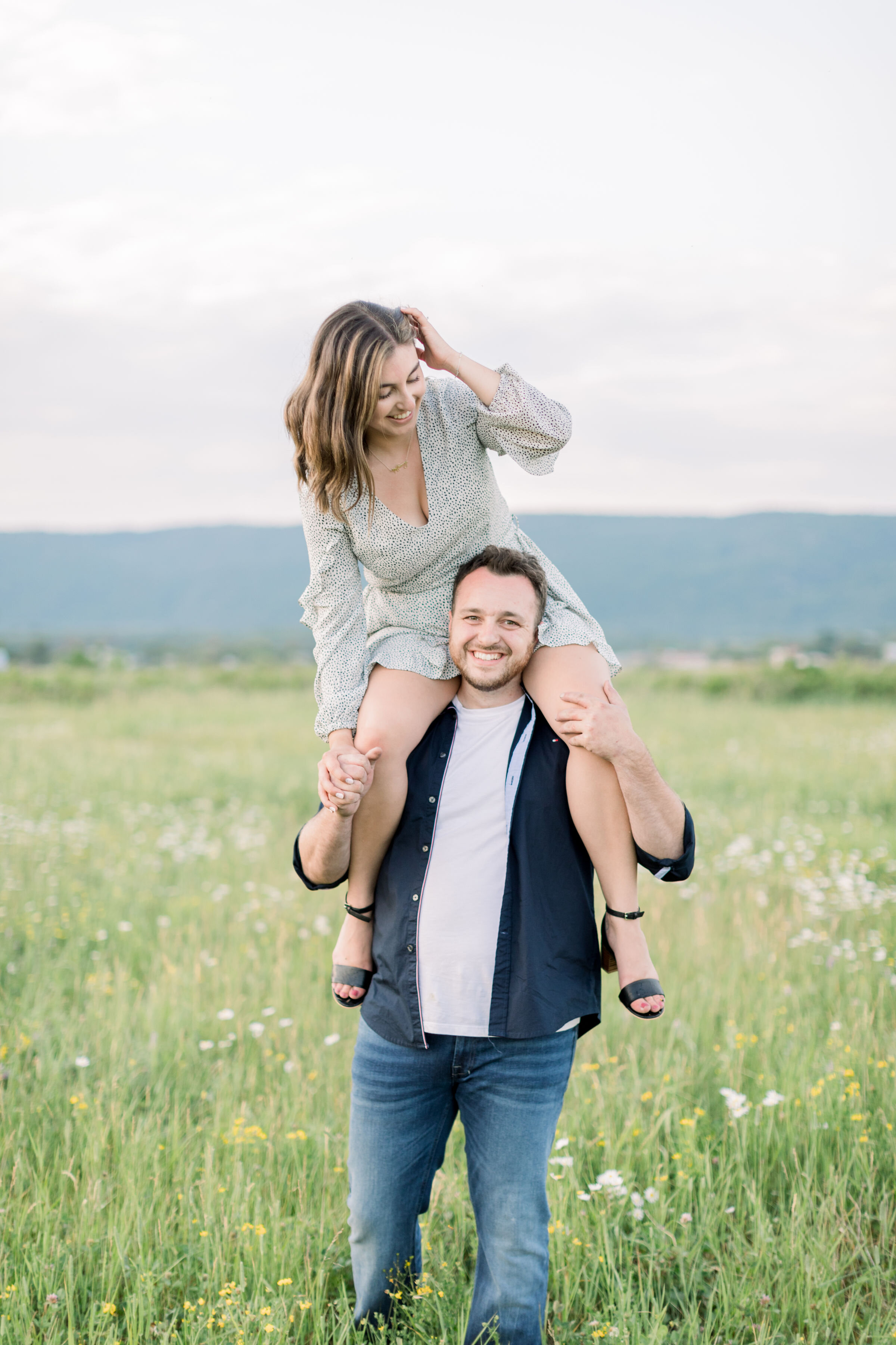  Cute couple with girl on boys shoulders in a green field in engagement photoshoot in Ottawa, ON by Chelsea Morgan Photography. engagement pose ideas posing inspo for engagements cute poses for couple photoshoot green field location in ottawa for pho
