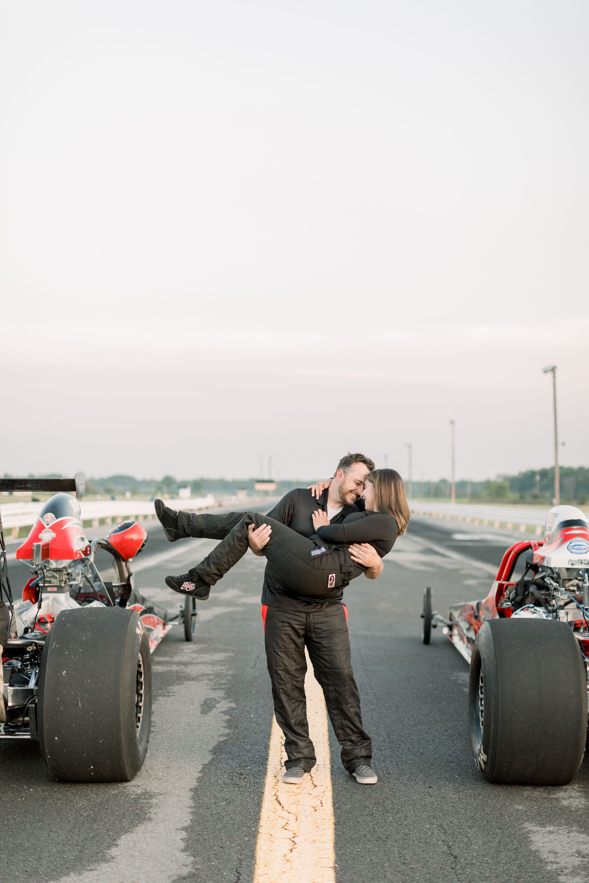 Unique engagement photos at a racetrack with racecar and couple in their racecar outfits in Ottawa, ON by Chelsea Morgan Photographer. best photographer in ottawa unique engagement photo ideas cars in engagement photos posing with cars racetrack loc