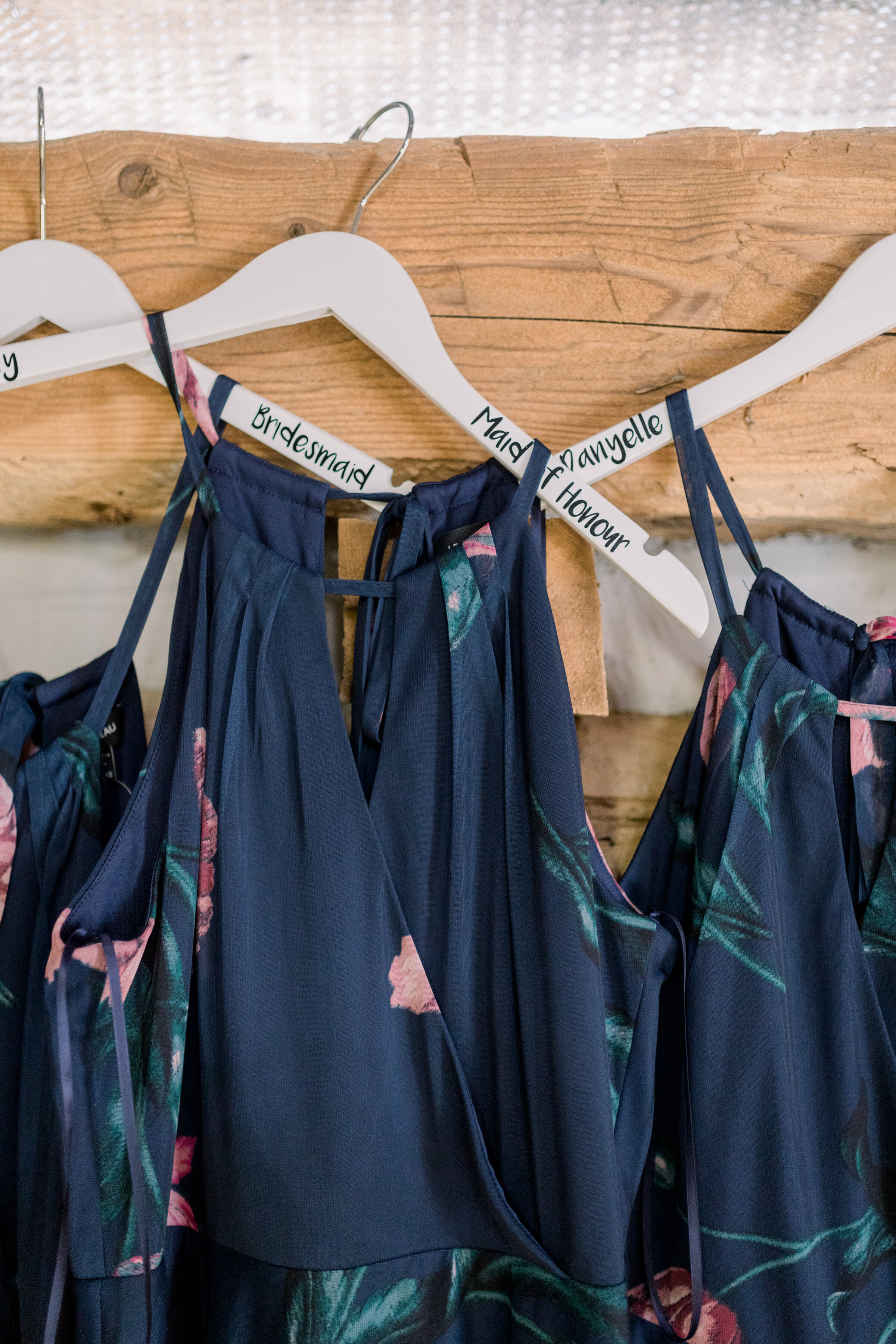  Beautiful navy and floral bridesmaids dresses hanging on custom made hangers with their names engraved on them by Chelsea Mason Photography in Ottawa, ON. bridesmaid outfit inspo what colors should my bridesmaids wear bridesmaid dresses how to style