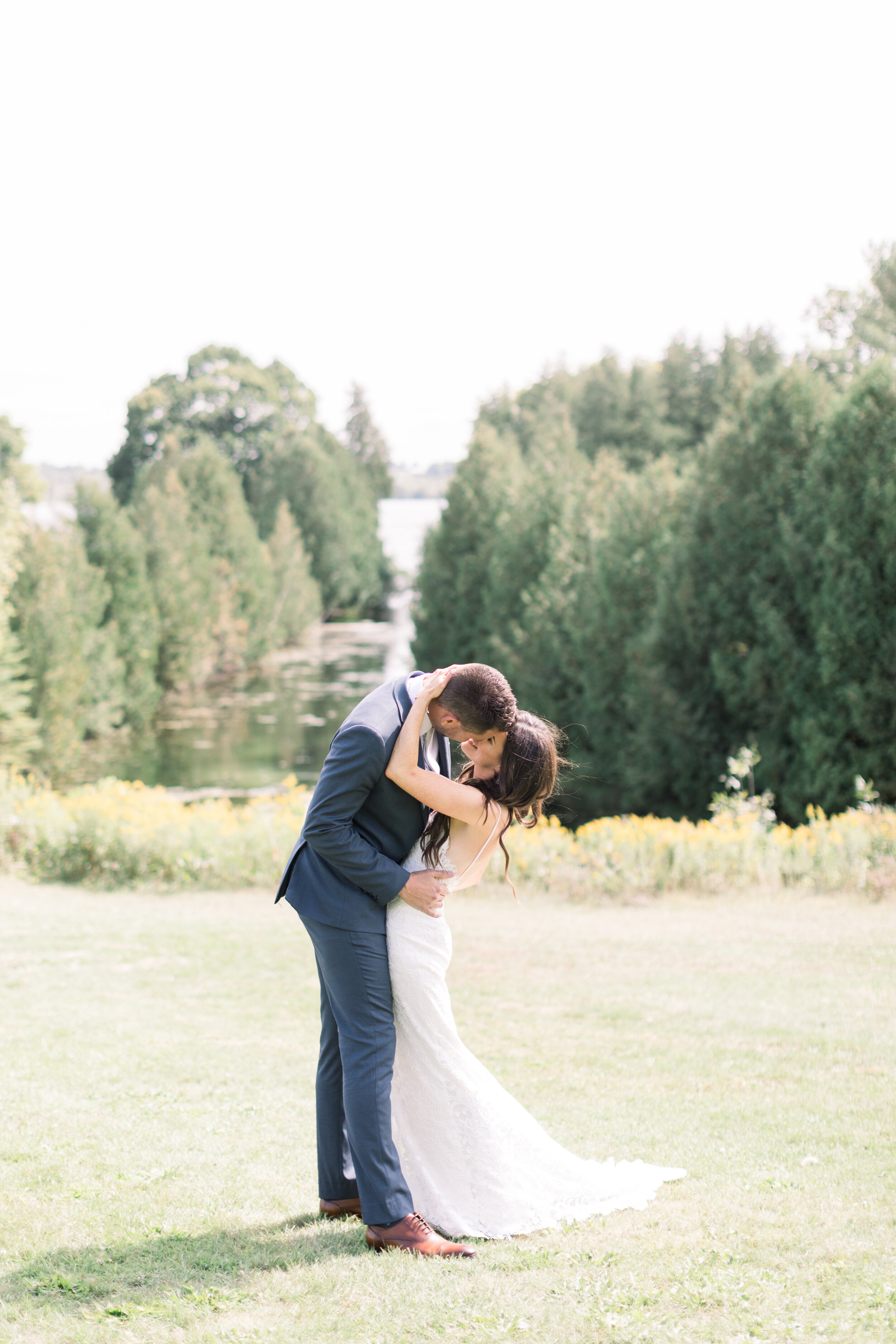  A bride and groom share a kiss before they walk down the aisle in their gorgeous backyard wedding in Kinmount, Ontario with Chelsea Mason Photography. Bride and groom pose wedding pictures inspo white dress summertime wedding outdoor Eganridge Resor